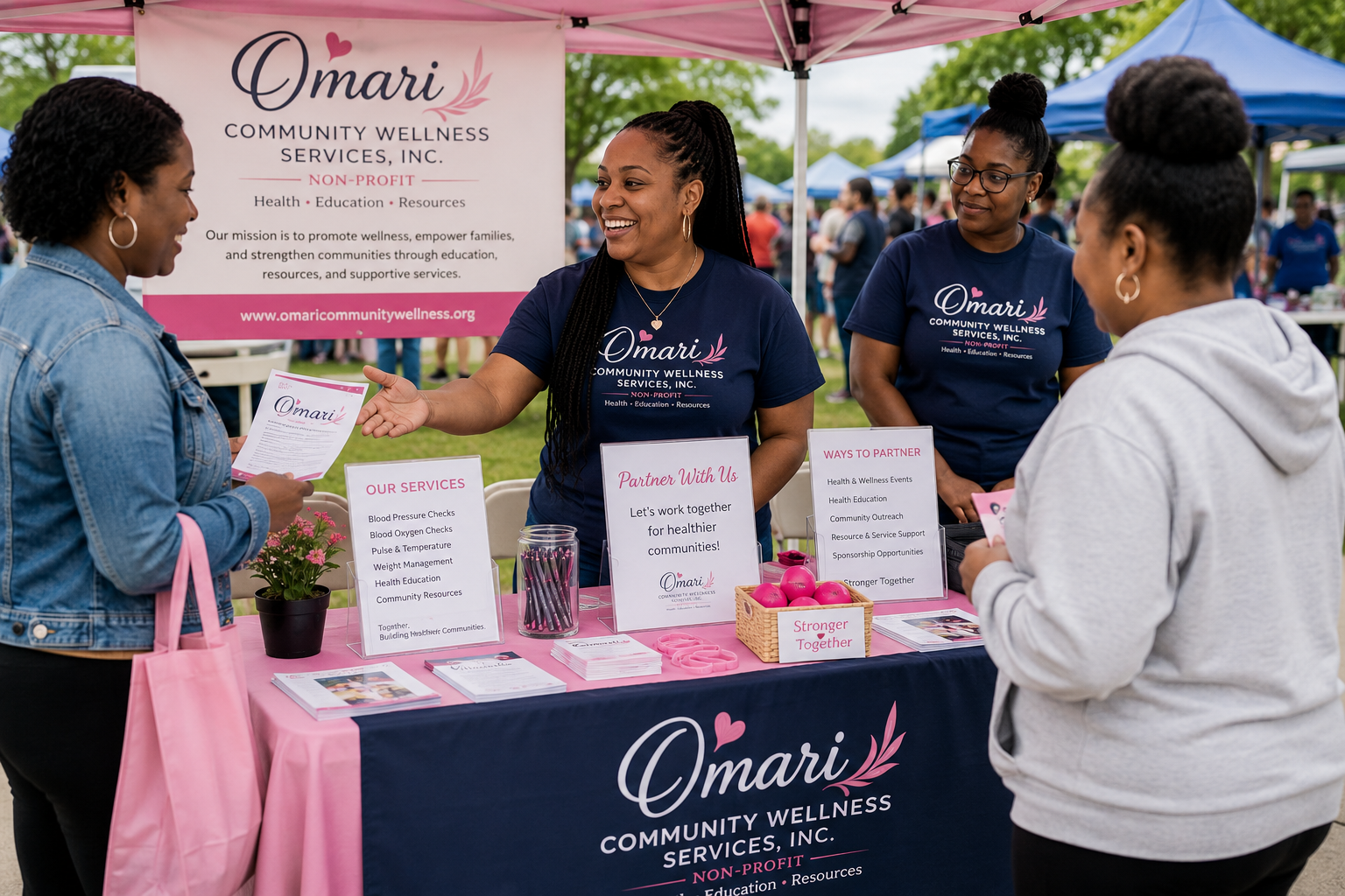 Community wellness event with two women at a booth for Omari Community Wellness Services, Inc., engaging with two attendees. Booth displays informative signs about health services and partnership opportunities, with a pink and blue canopy setup outdoors among other tents and people.