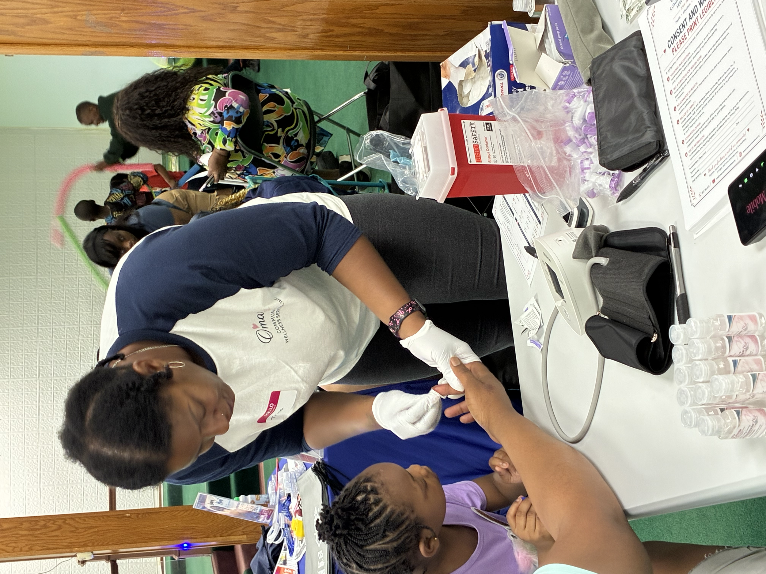 People sitting at a table participating in a health or vaccination event, with medical supplies and informational materials on the table.