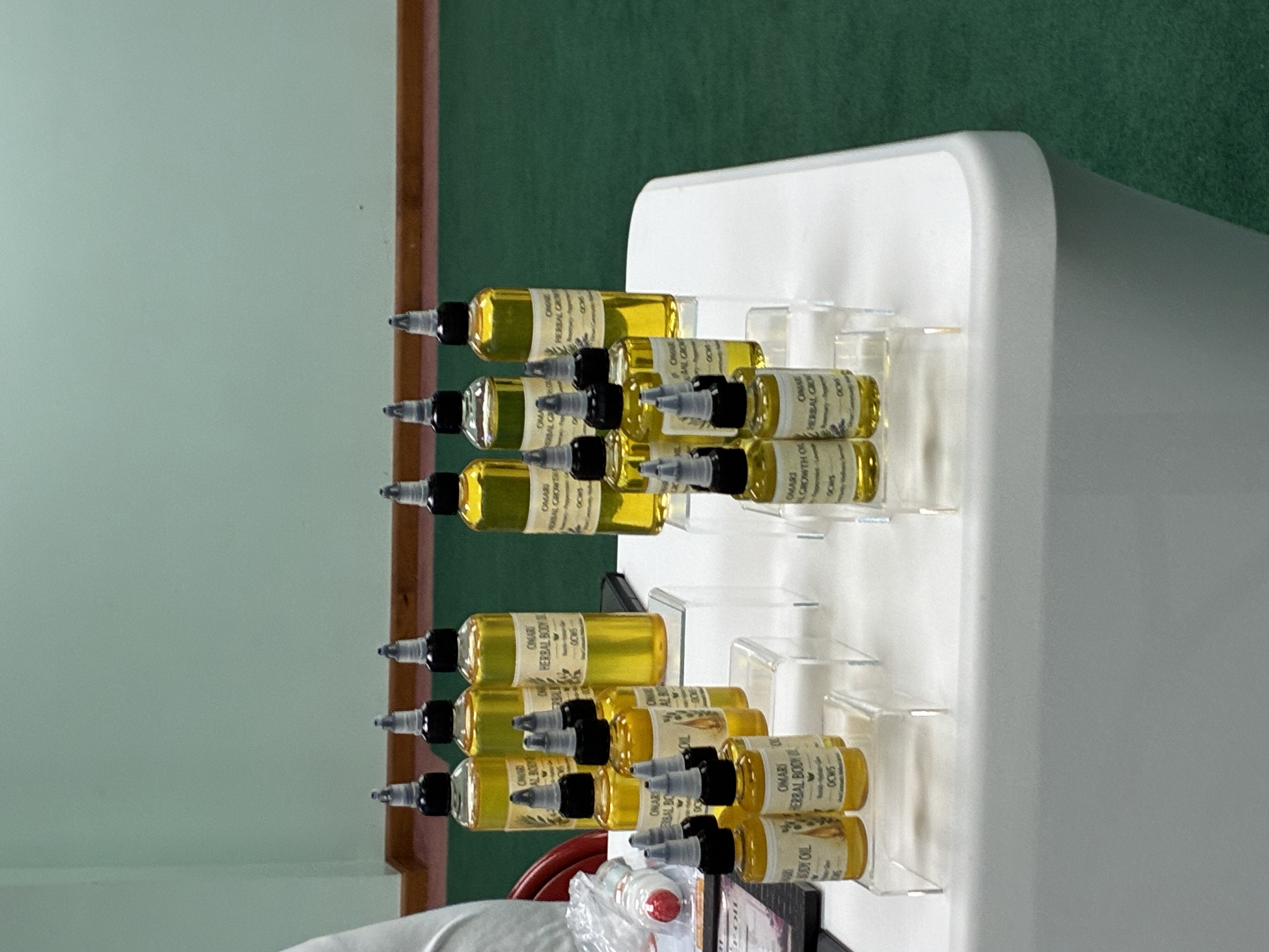 A display of small bottles filled with a yellow liquid, arranged in rows on a table, each with a black nozzle cap and labeled with a white and beige sticker.