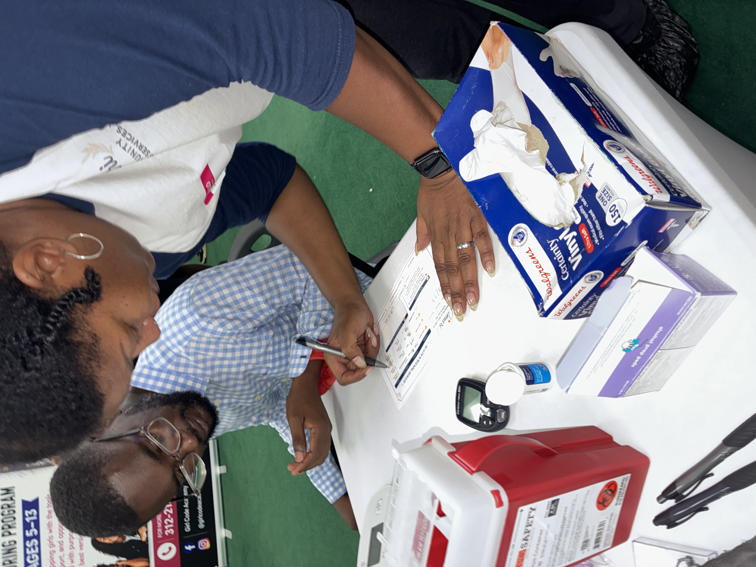 People gather around a table looking at blood donation supplies and informational materials at a blood drive event.