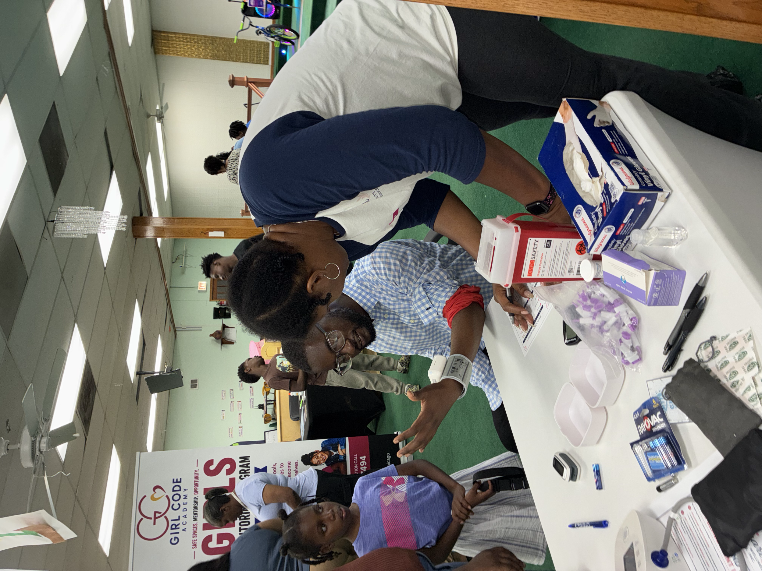 People at a youth program registration booth with informational banners, tables with various items, and attendees engaging with the representatives.