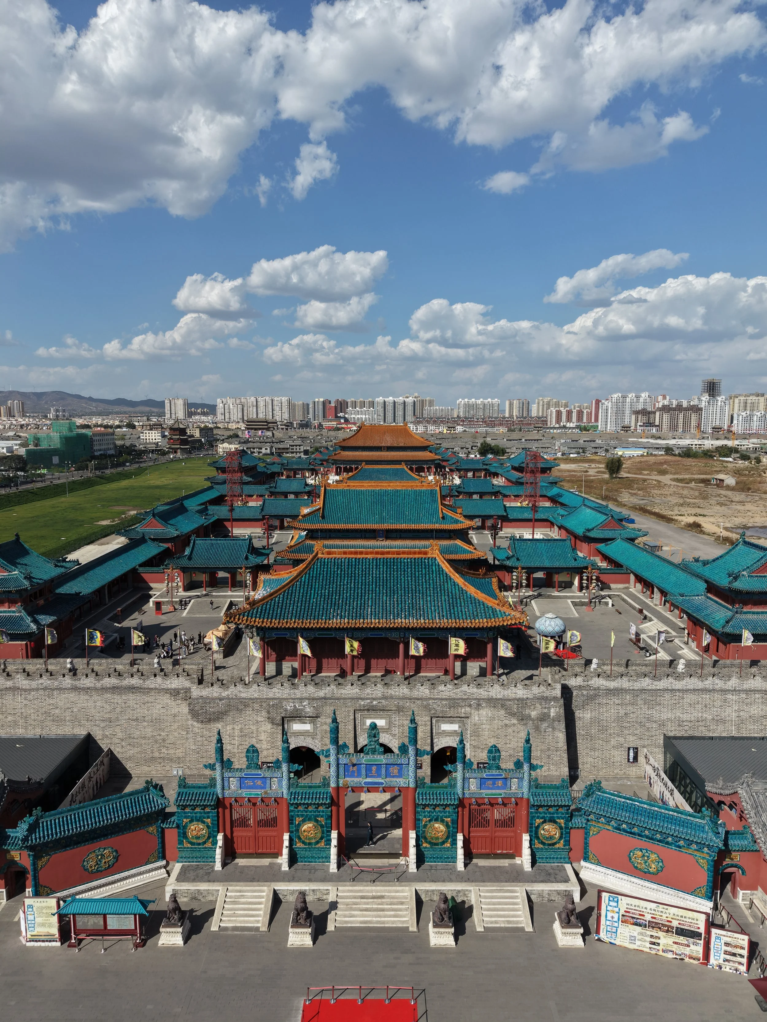 A traditional Chinese temple with colorful rooftops and intricate architecture, set against a modern cityscape with high-rise buildings and a partly cloudy sky.