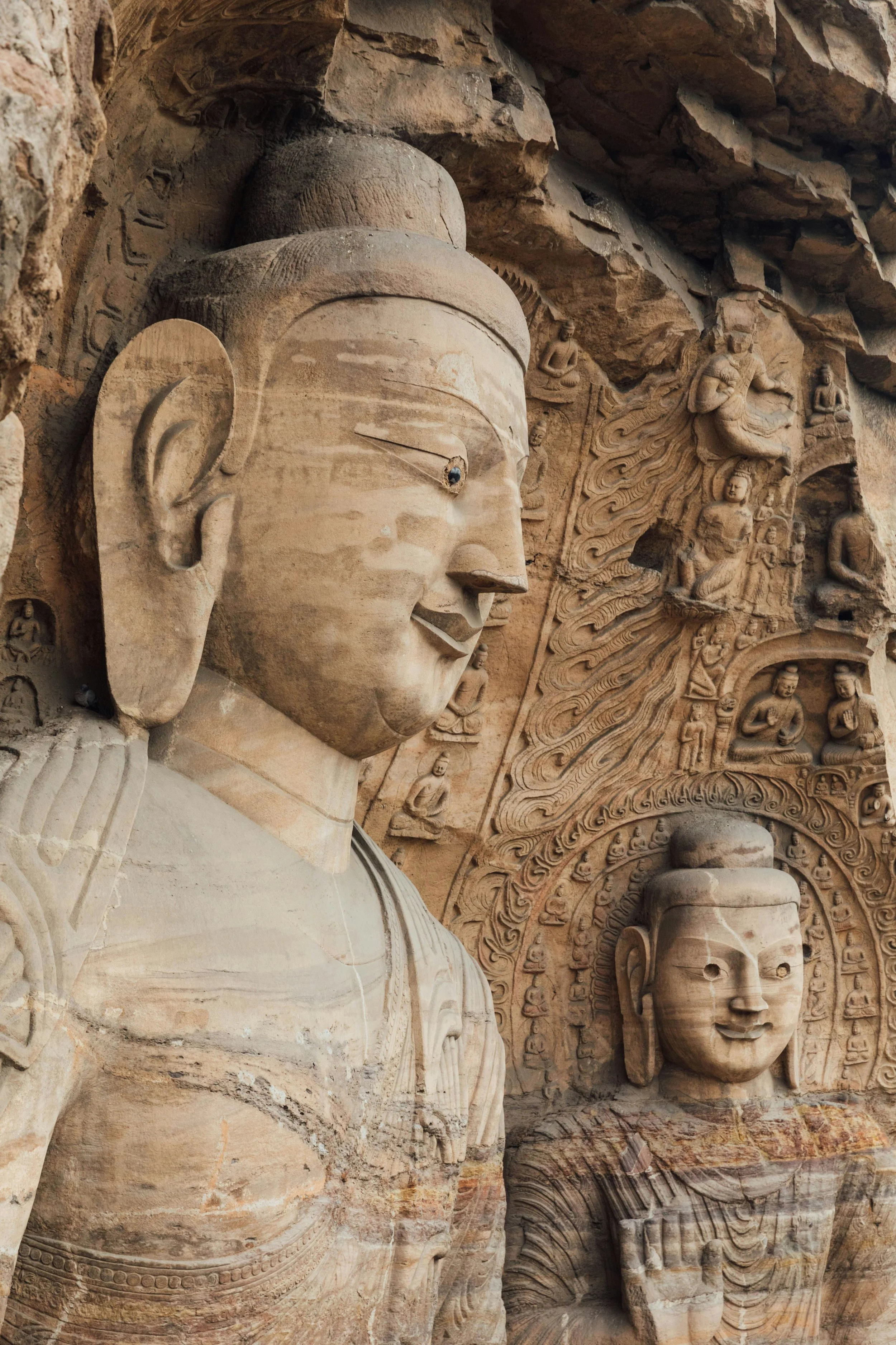 Ancient stone sculptures of Buddha and other figures carved into a cliff face, with detailed bas-reliefs surrounding them.
