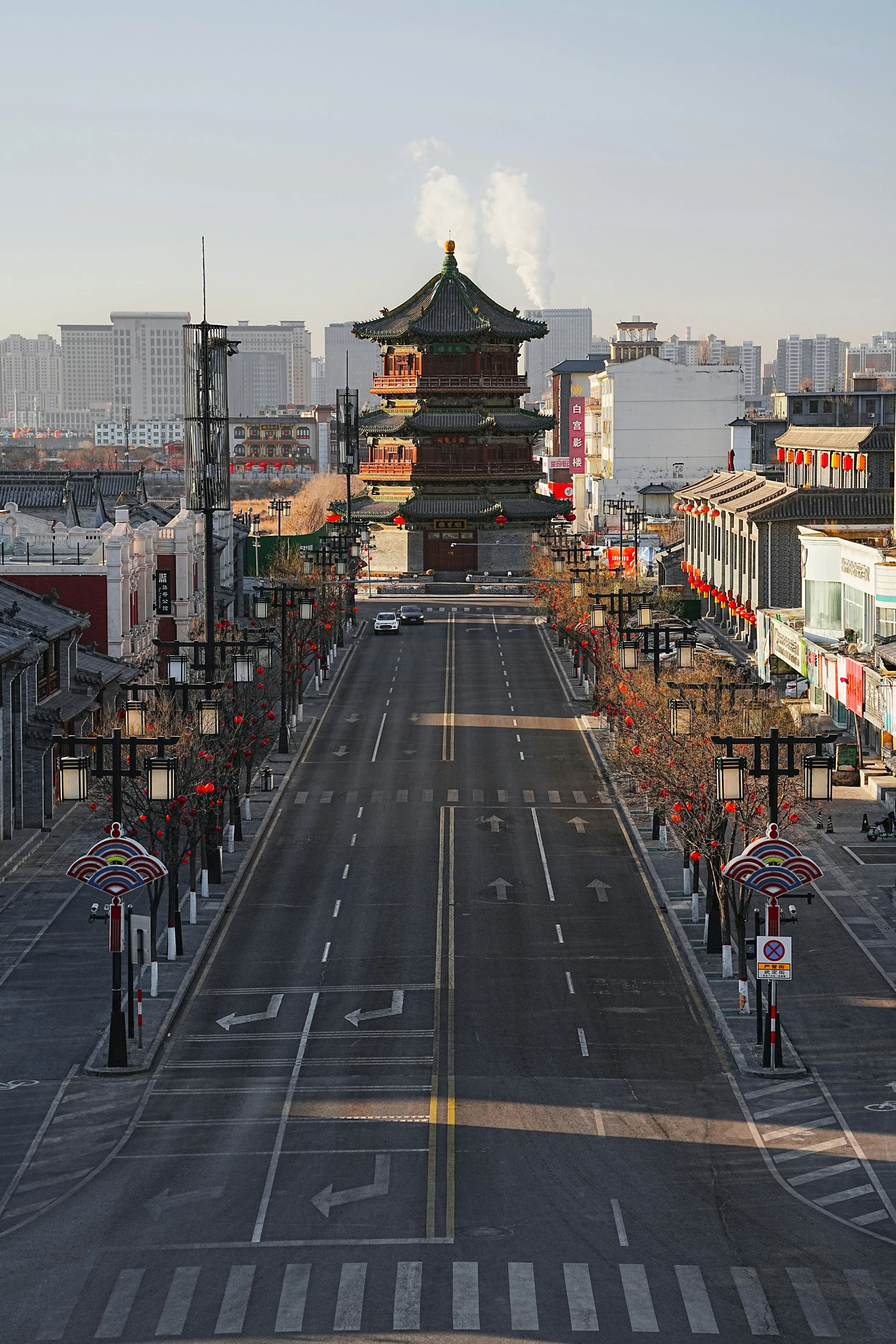 Empty street with traditional Chinese buildings on either side and a pagoda-style building in the background, decorated with red lanterns and trees with red ornaments.
