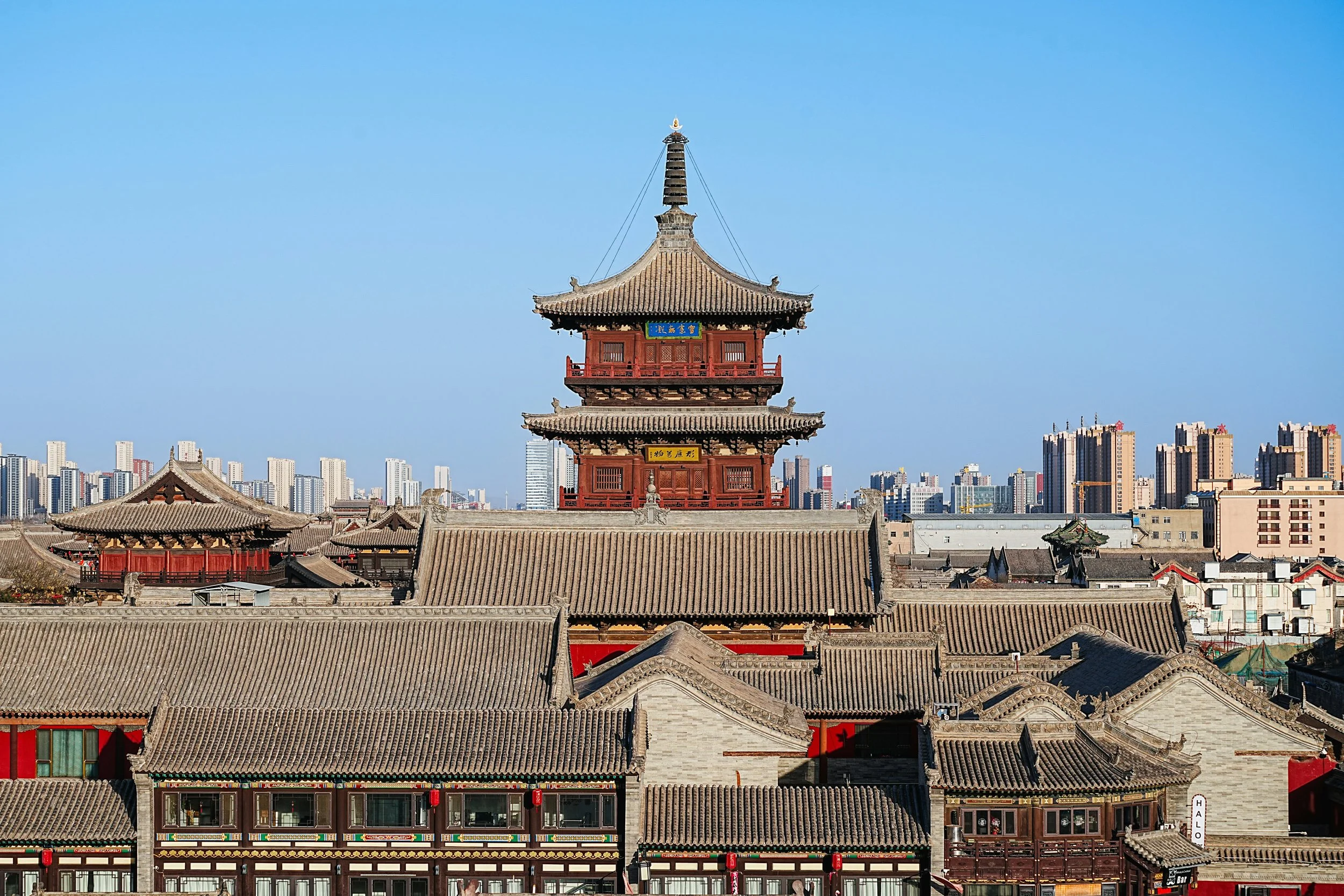 Traditional Chinese pagoda with multiple roofs, set against a modern city skyline with tall buildings in the background.