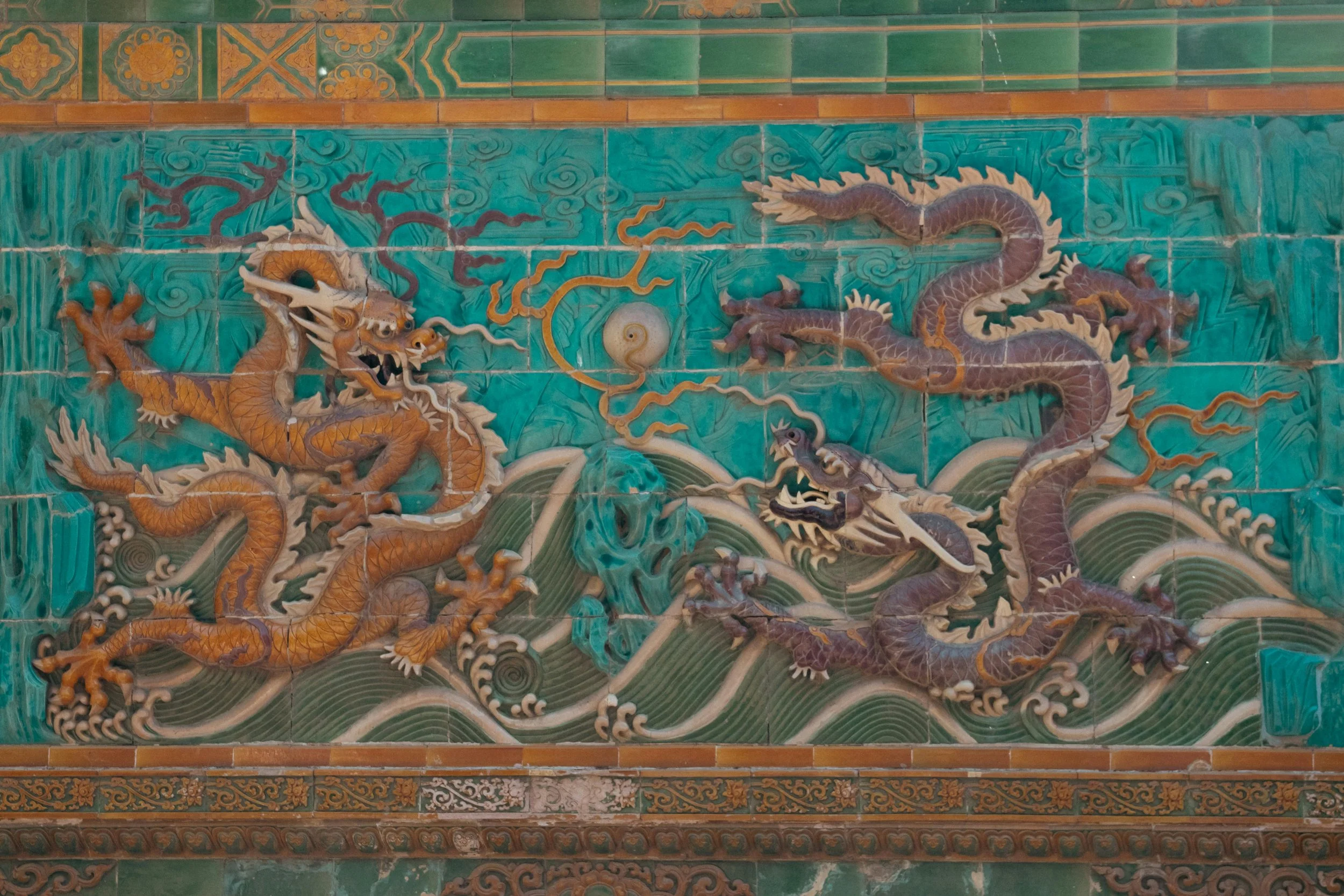 A decorative tile mural depicting two Chinese dragons in a fierce encounter surrounded by waves, clouds, and celestial elements.