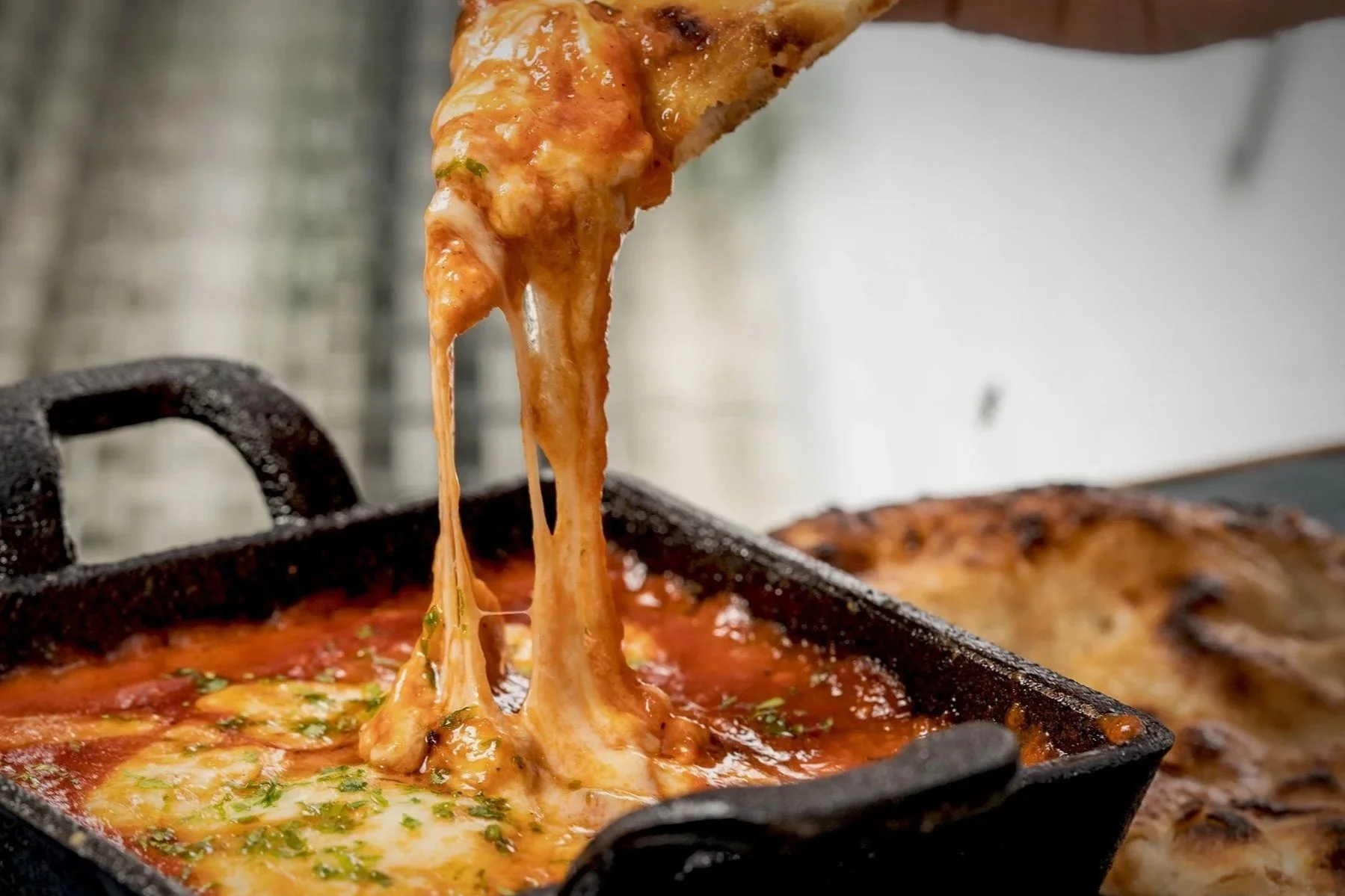 A slice of bread  being lifted from a black skillet, with melted cheese stretching from the slice to the rest of the bread