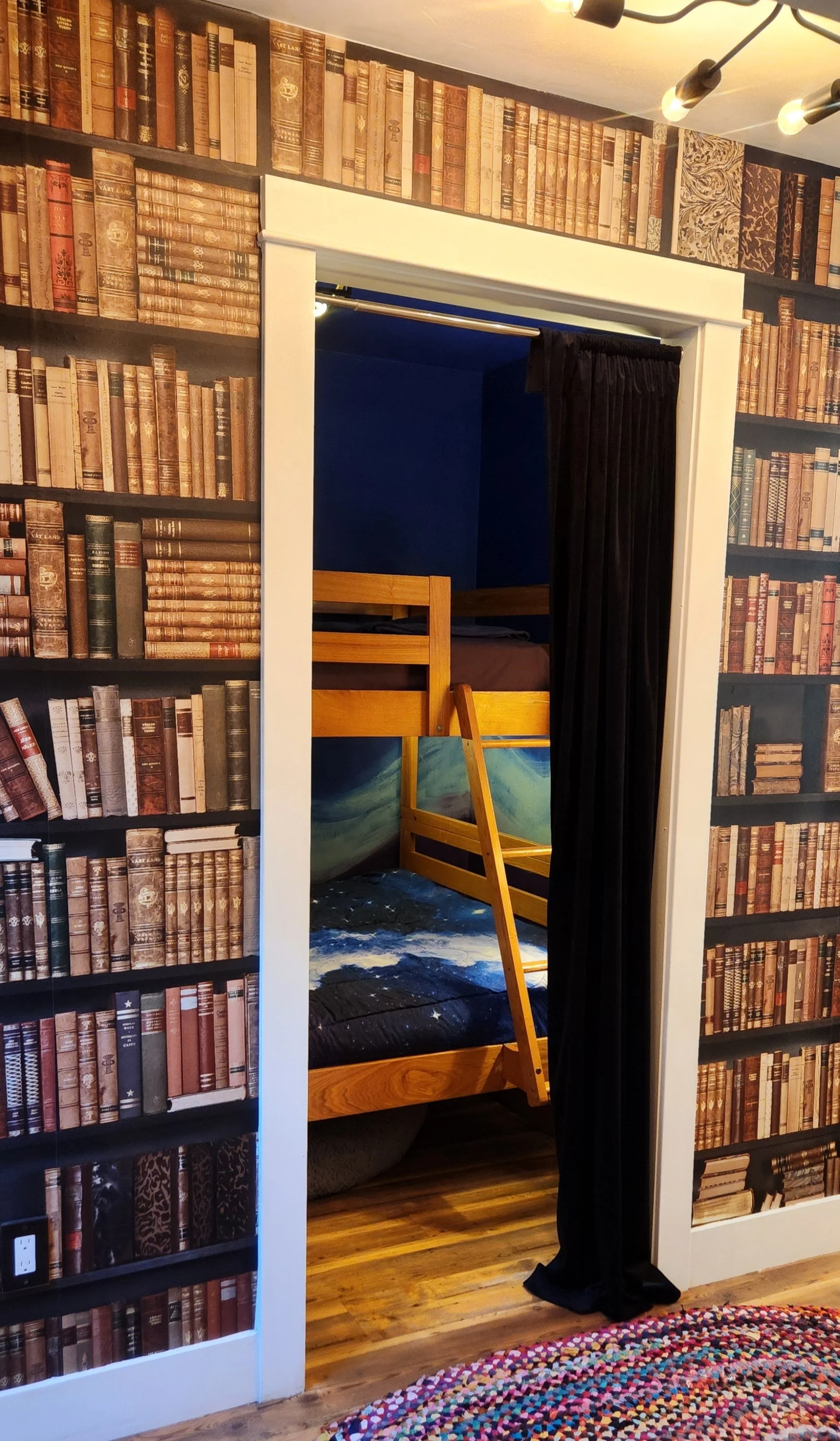 View of a doorway with black curtains leading to a room with blue walls and a wooden bunk bed inside.