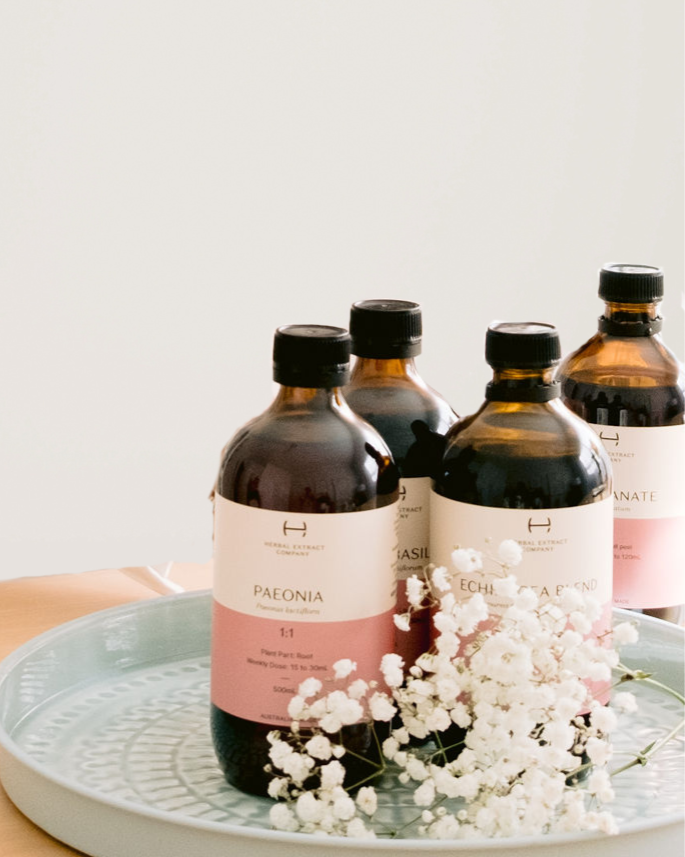 Four amber glass bottles with black caps and white labels arranged on a light blue dish, decorated with white baby's breath flowers, on a wooden surface.