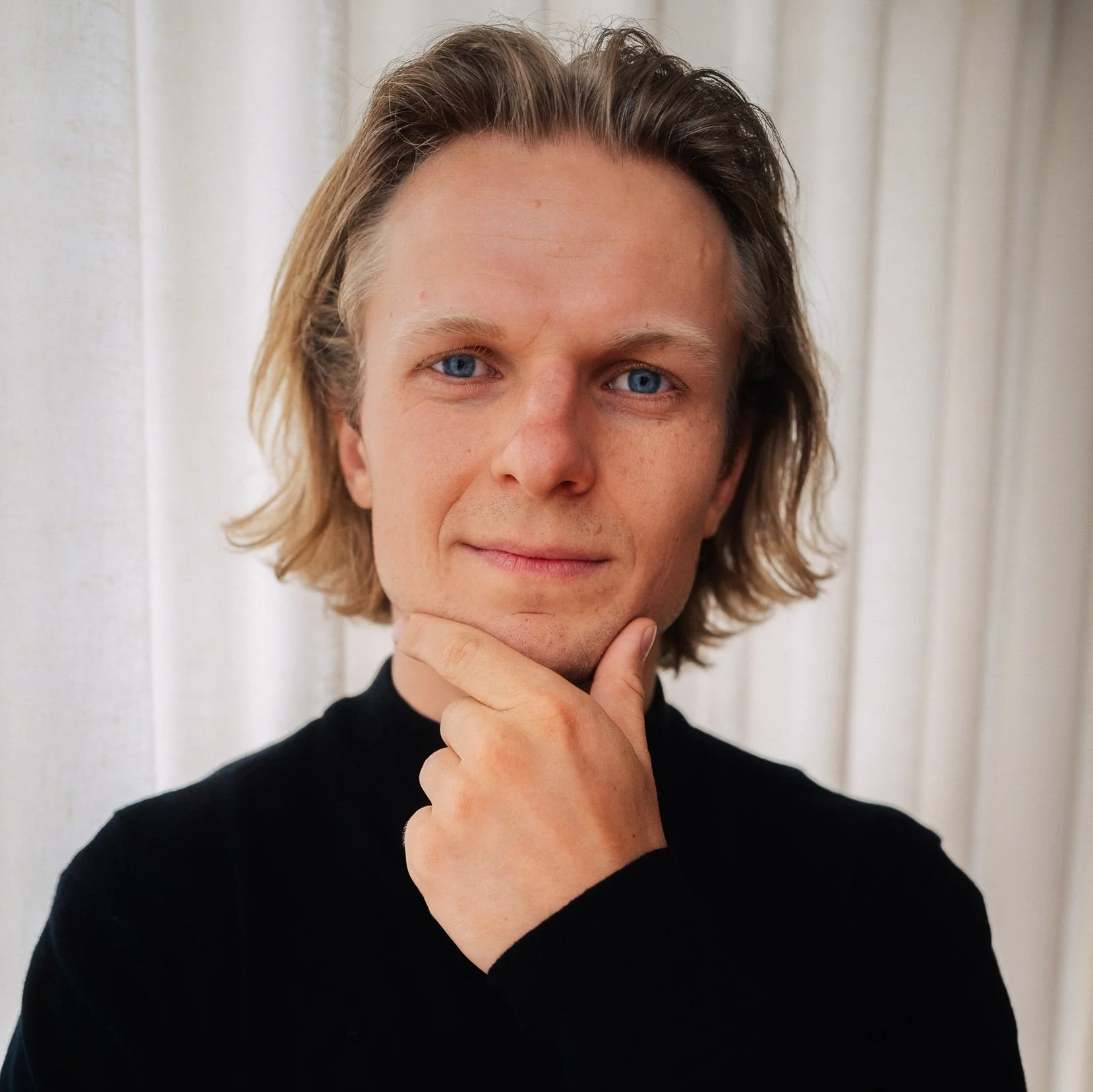 A man with brown hair wearing a light blue collared shirt, smiling at the camera.