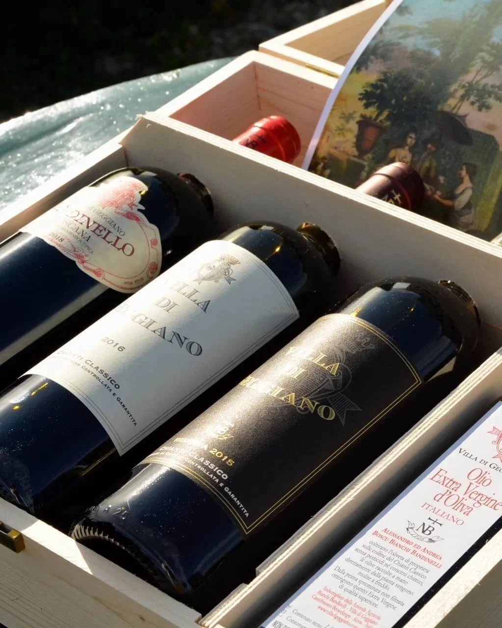 Three bottles of Italian wine in a white wooden box, with one bottle labeled 'Luna di Giano' from 2016 and another from 2015, with a backdrop of a colorful booklet or brochure.