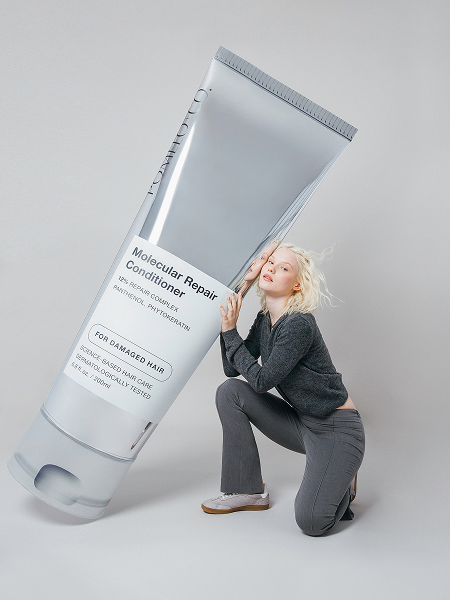 Woman kneeling next to a giant tube of molecular repair conditioner for damaged hair.