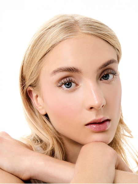 Close-up of a young woman with blonde hair and blue eyes resting her chin on her hand.