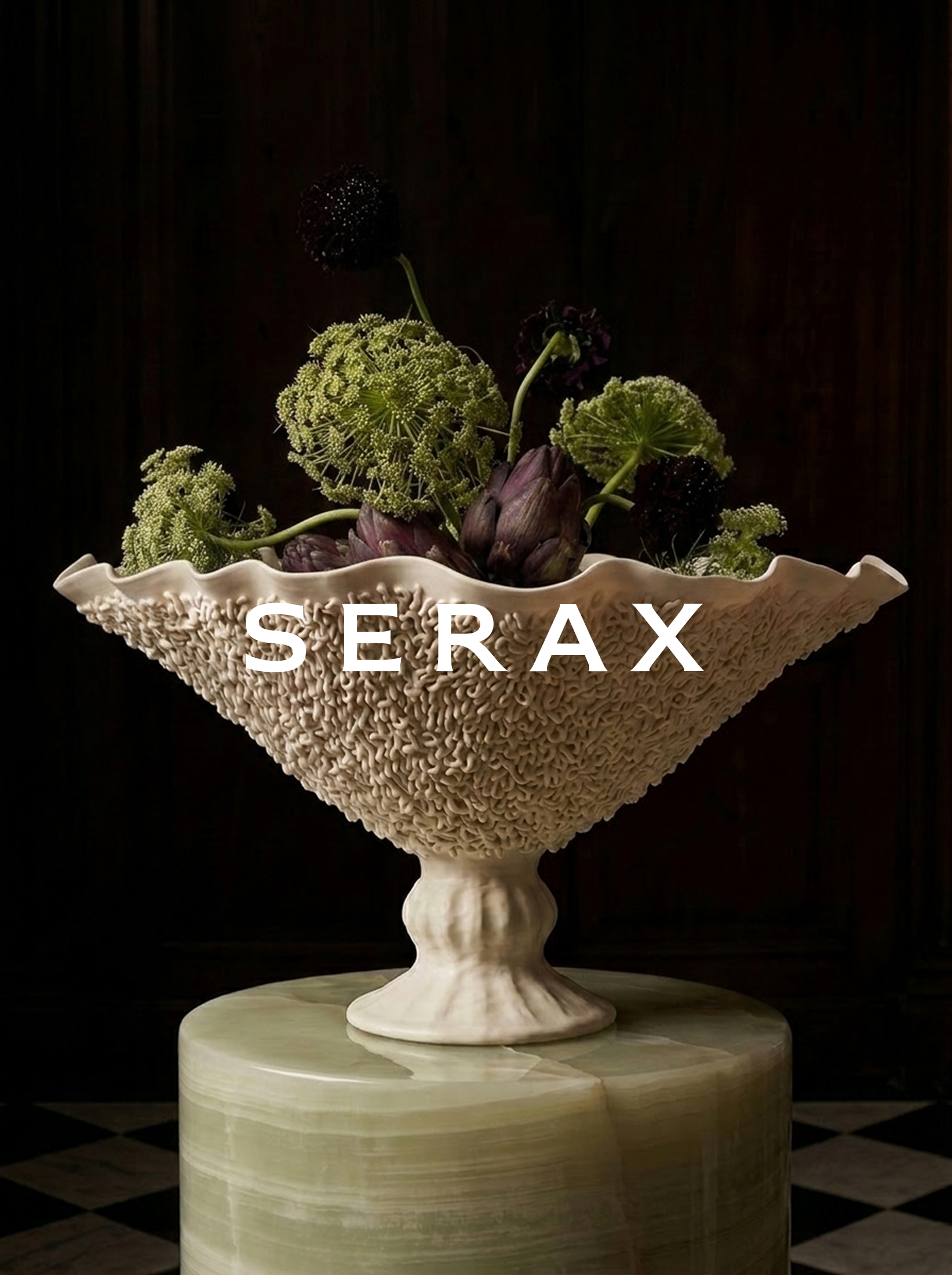 A decorative ceramic bowl with a textured exterior and intricate floral patterns, filled with an arrangement of artichokes and green flowering plants, set on a marble pedestal against a dark background.