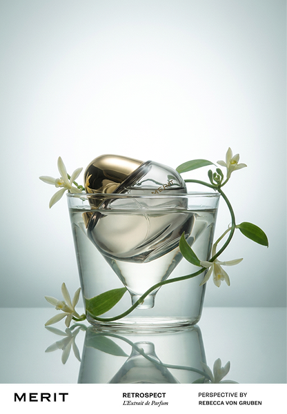 A perfume bottle submerged in a glass of water with white flowers and green leaves for decoration.