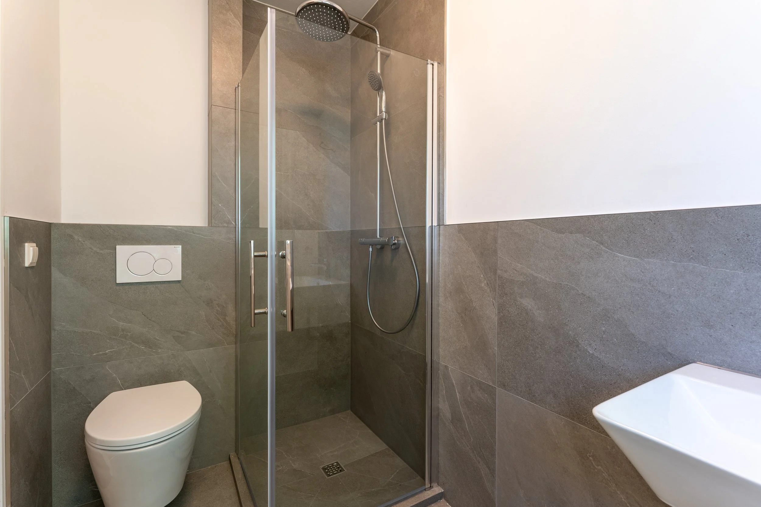 Modernes Badezimmer mit begehbarer Dusche, Wandtoilette und Waschbecken.