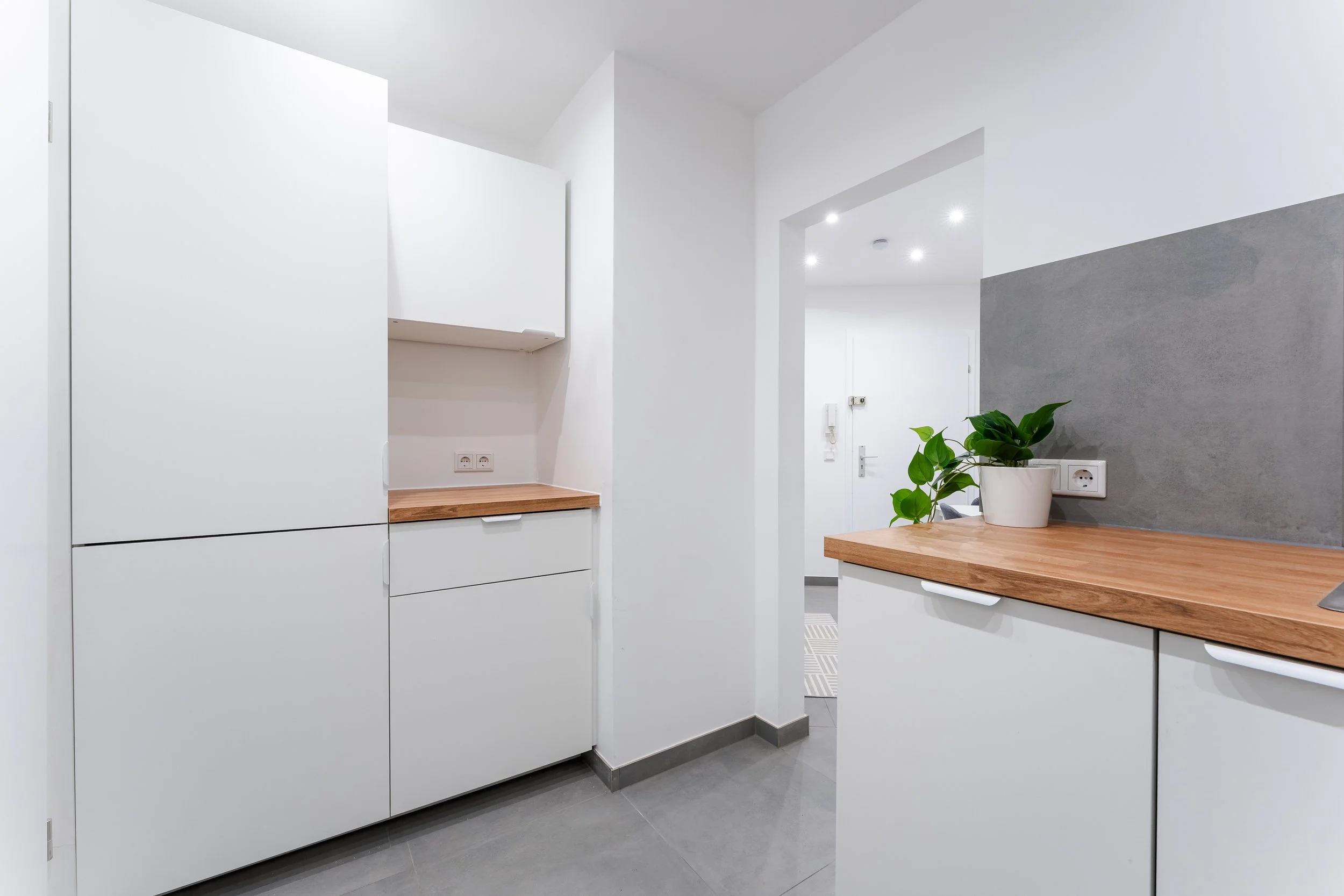 Moderne, minimalistische Küche mit weißen Schränken, Holzarbeitsflächen und grüner Pflanze