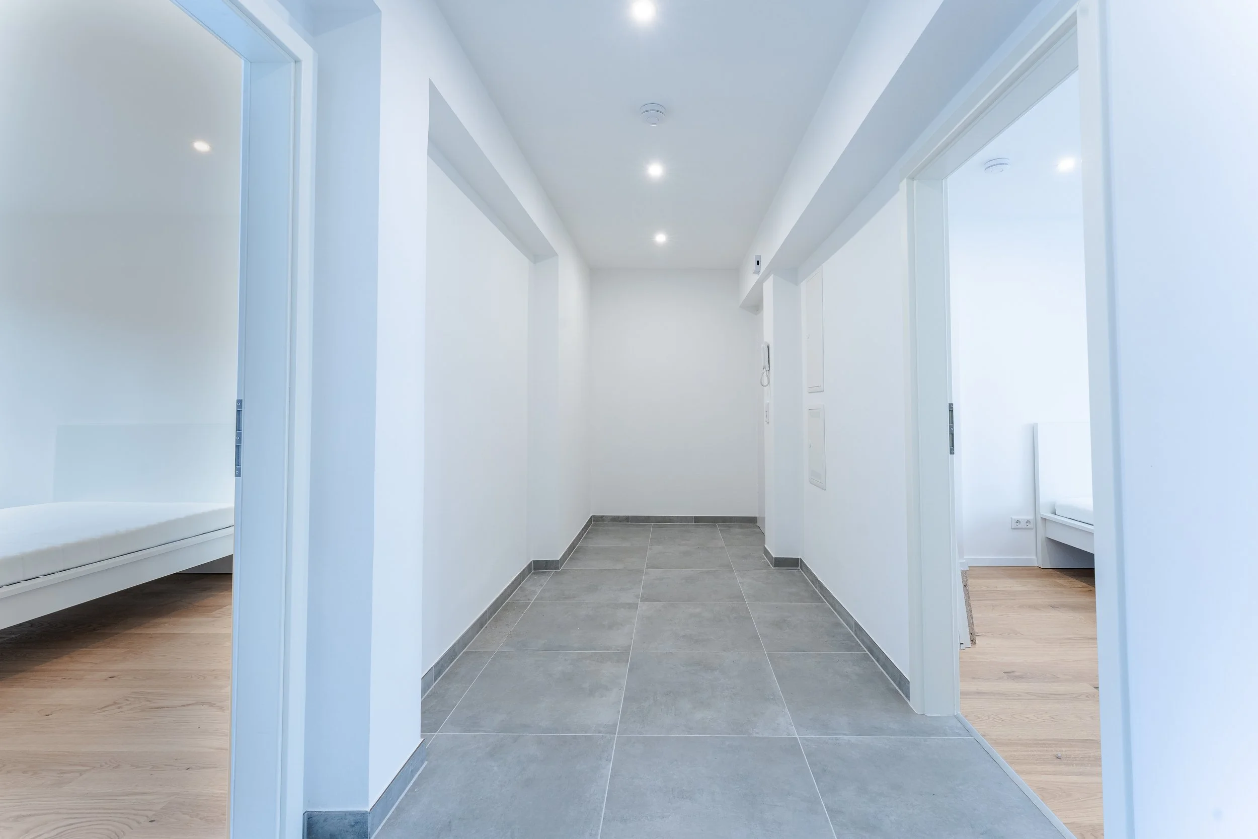 Leeres Flur in einer modernen Wohnung mit grauem Fliesenboden und weißen Wänden.
