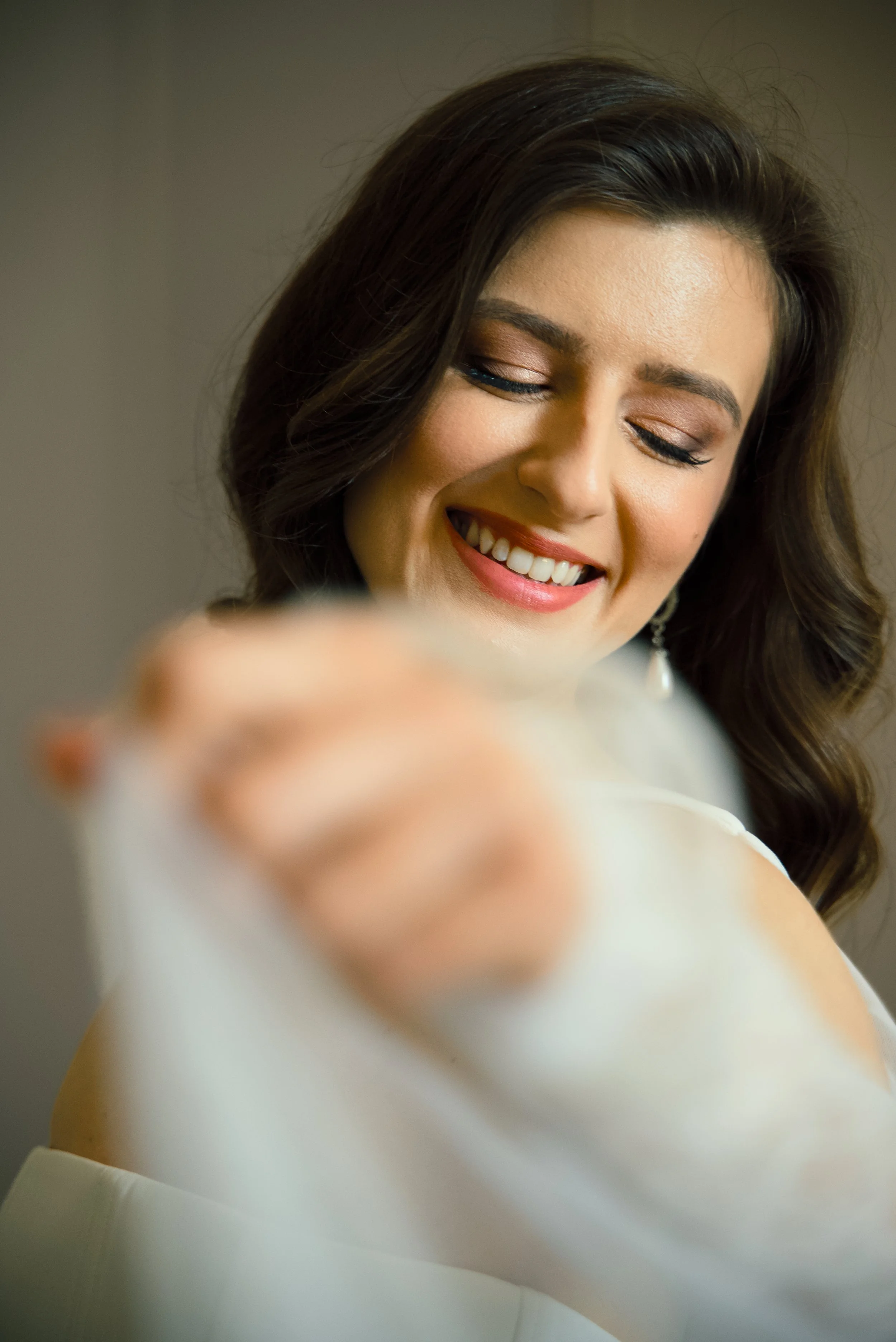 A woman smiling and pointing towards the camera, with a focus on her face and a blurred hand in the foreground.