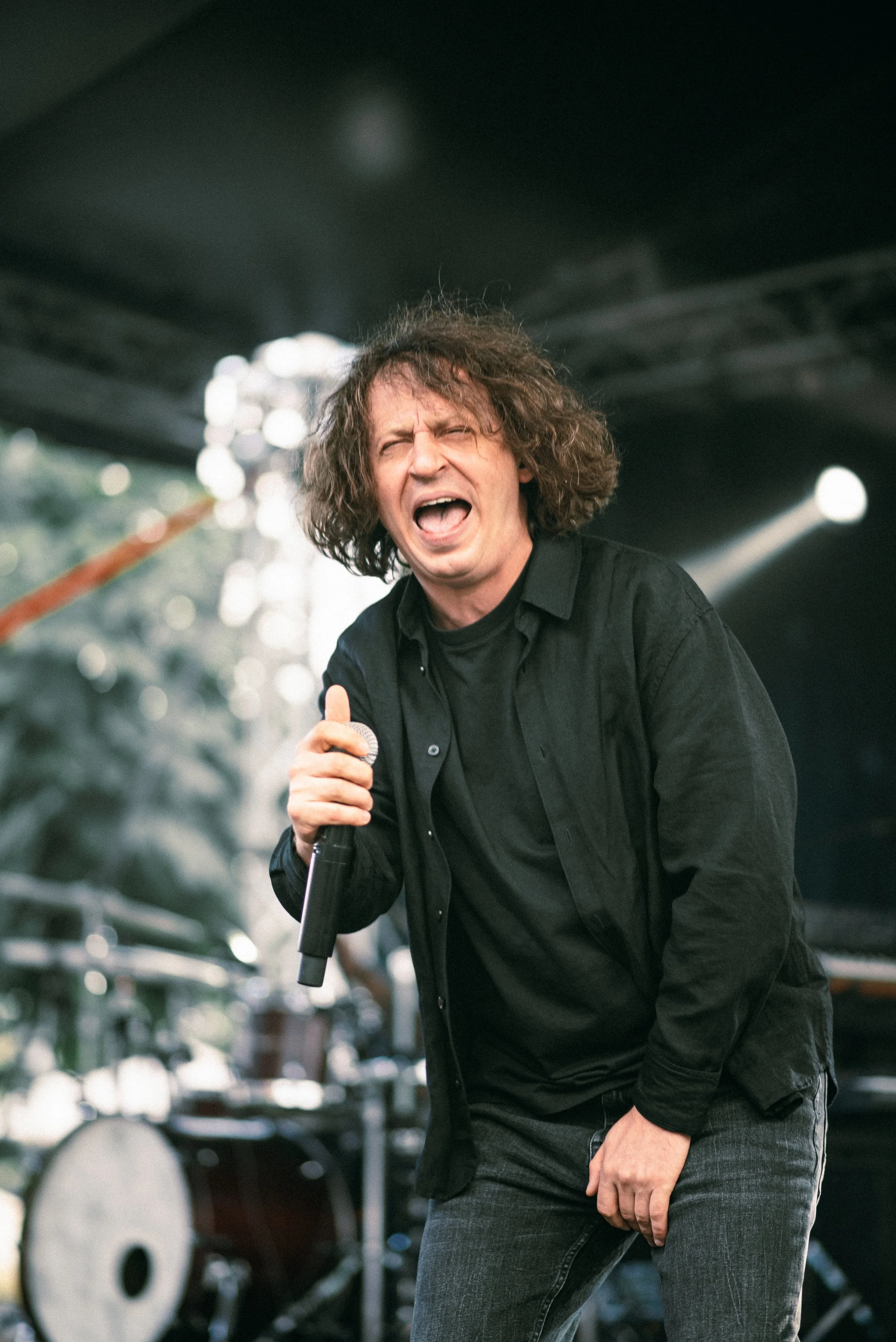 A man singing passionately into a microphone during a live outdoor music performance.