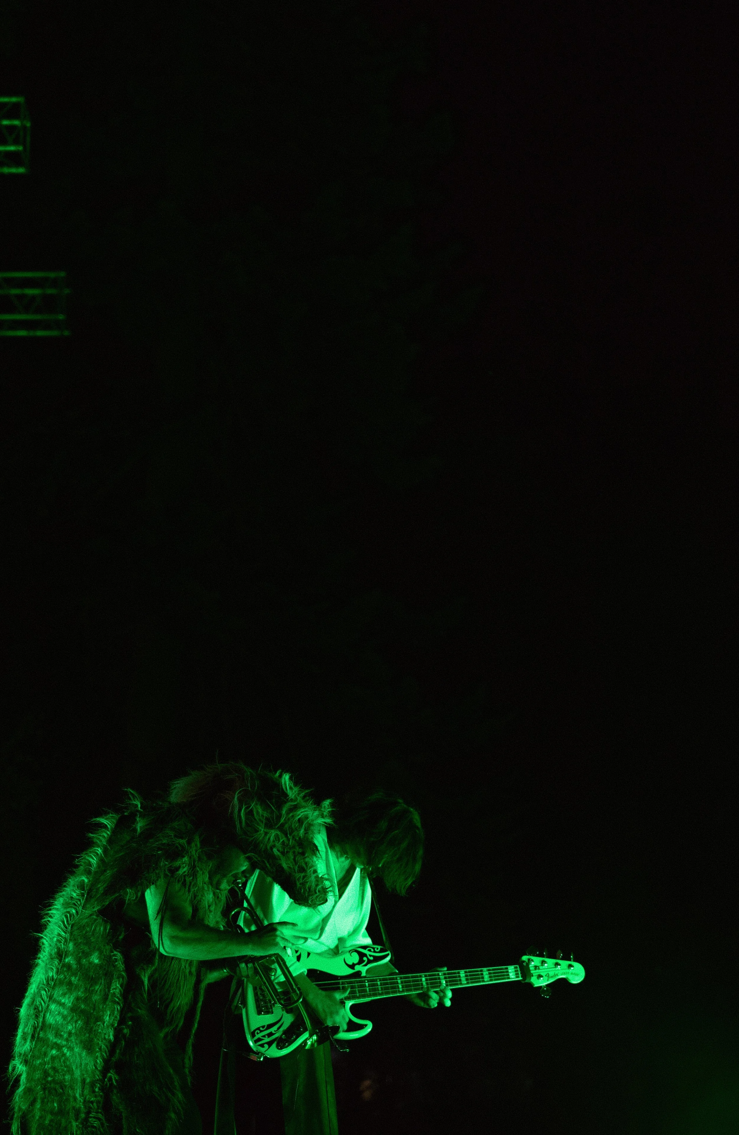 Two musicians playing guitars on stage under green lighting.