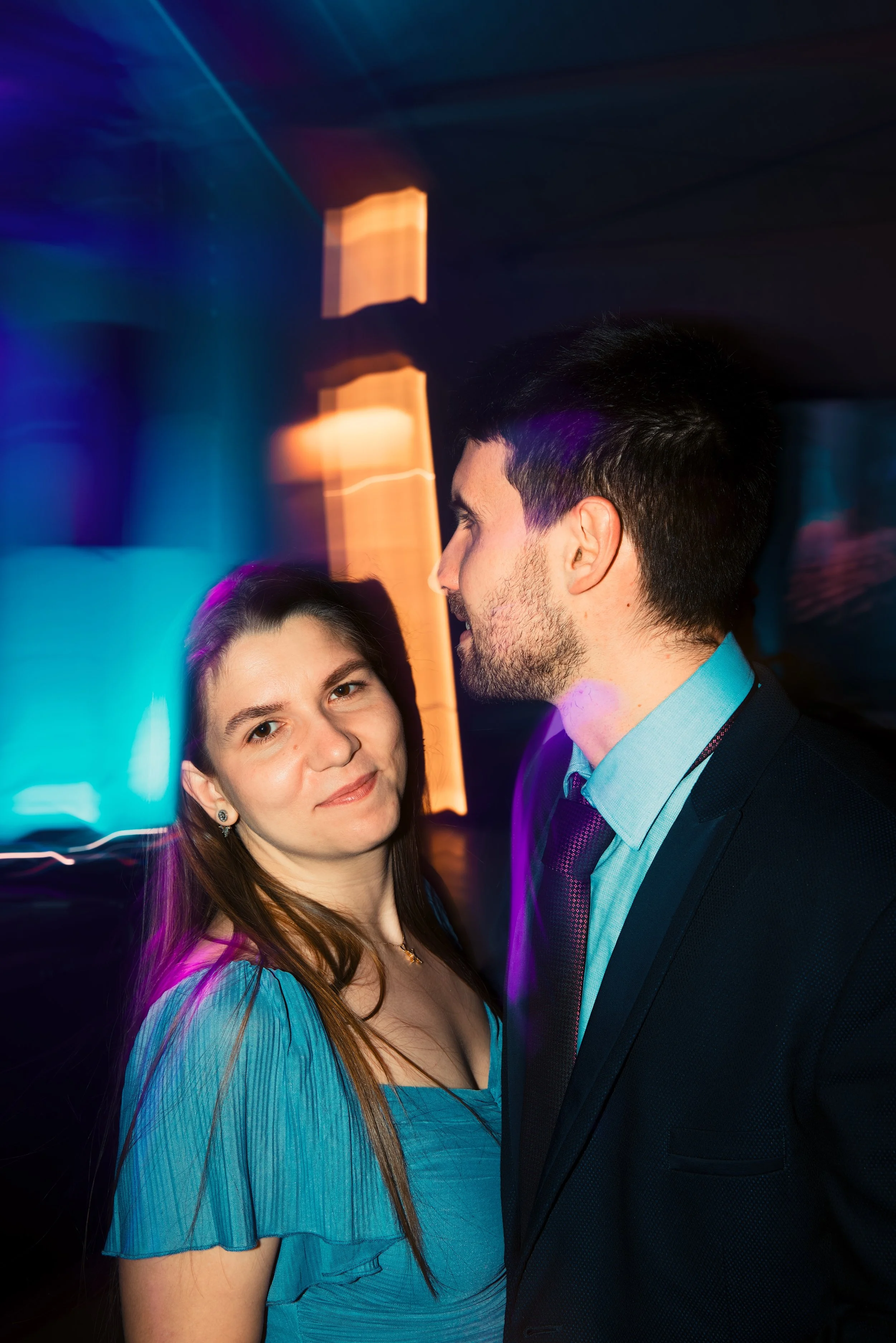 A man and woman at a party or nightclub with colorful, blurred lights in the background.