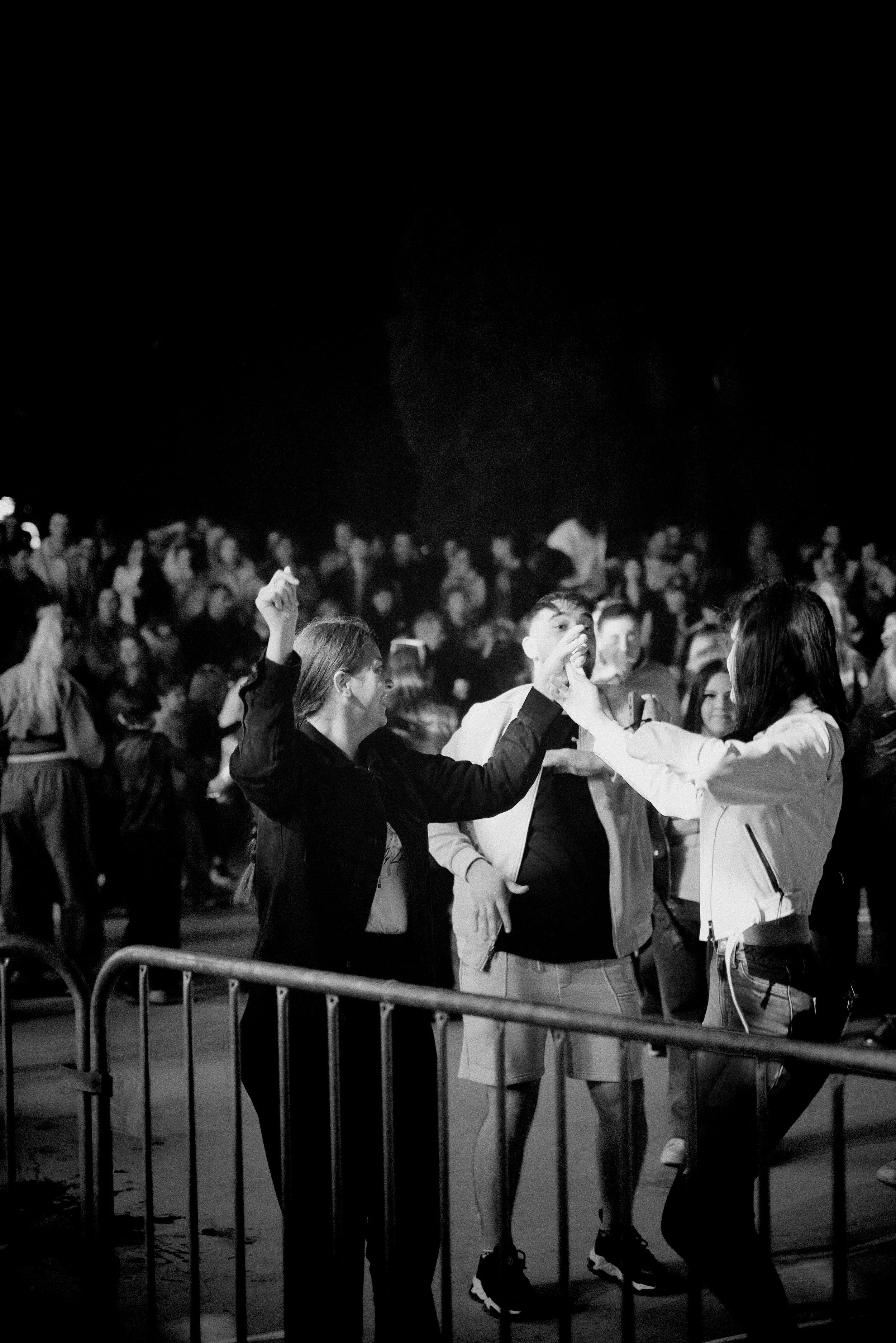 People dancing at a nightclub or concert in black and white, with a crowd in the background.