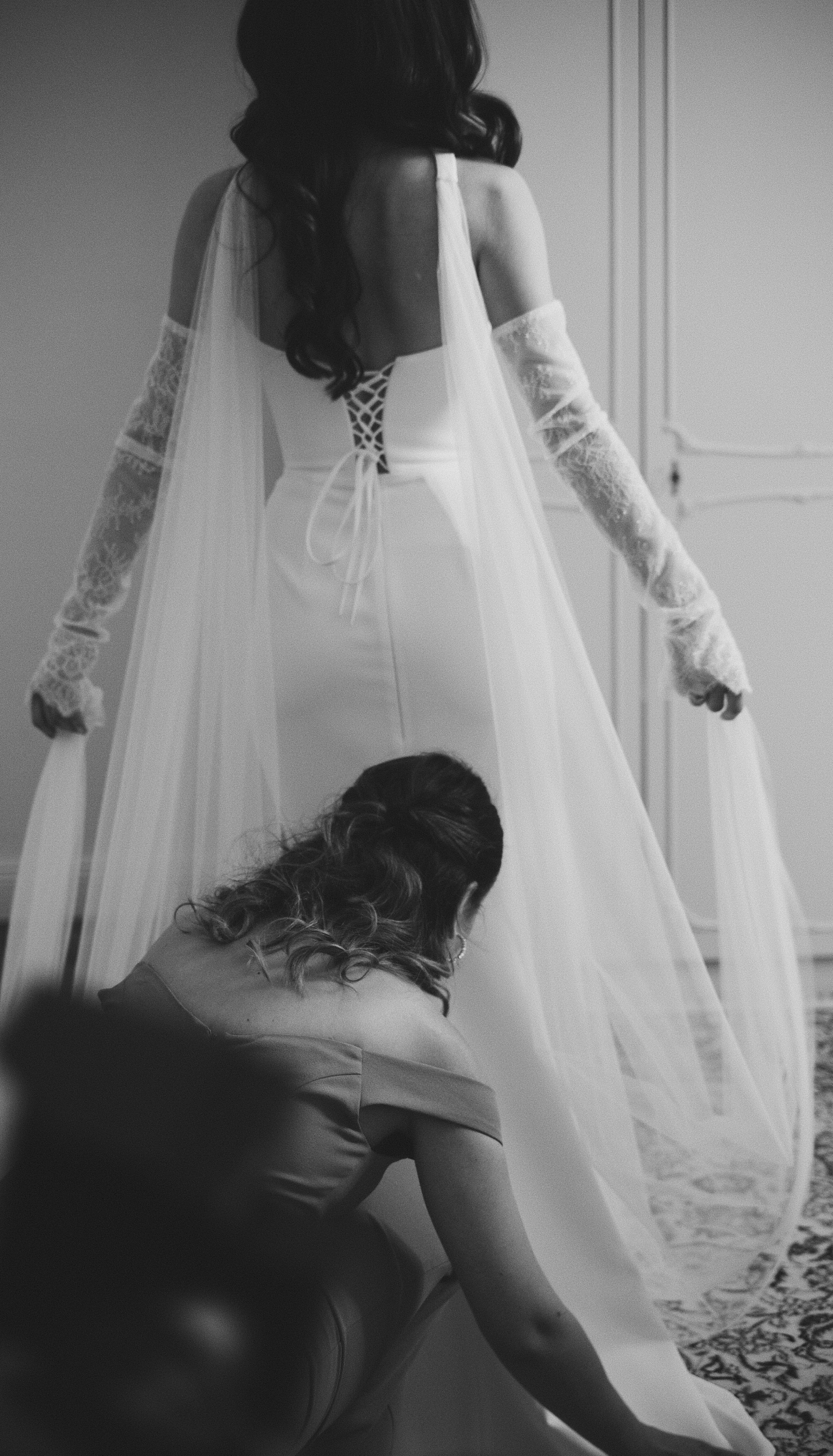Woman kneeling to adjust bride's dress, black and white photograph