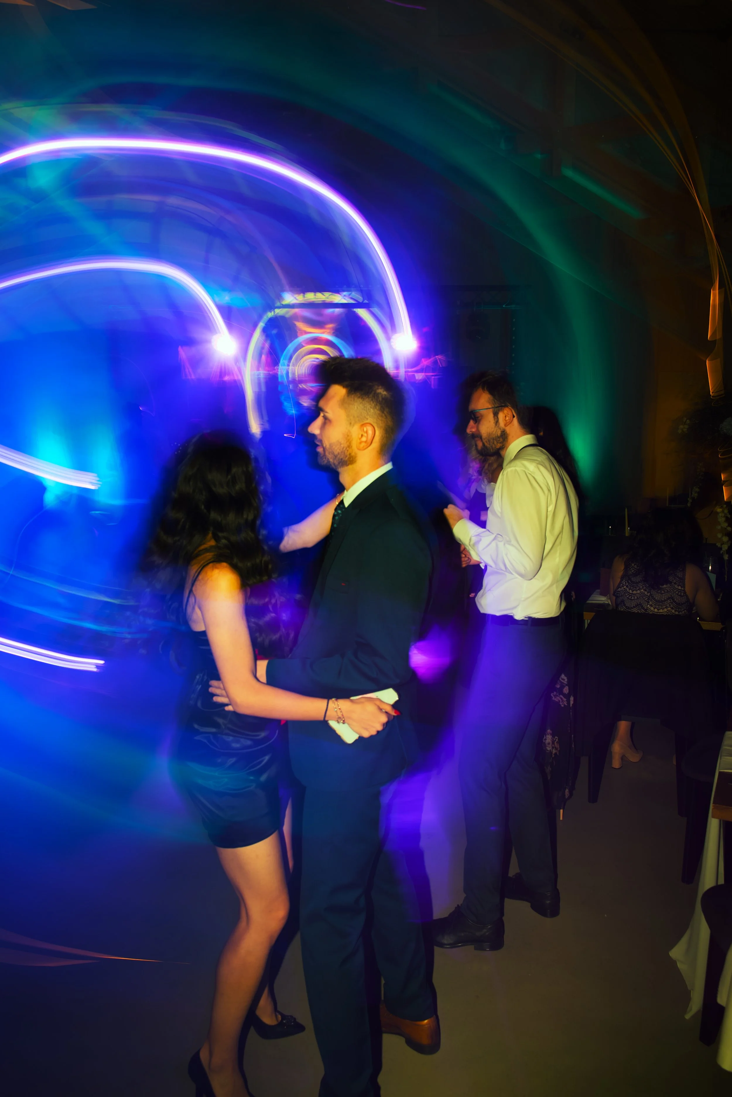 Couple dancing at a party with colorful swirling lights in the background.