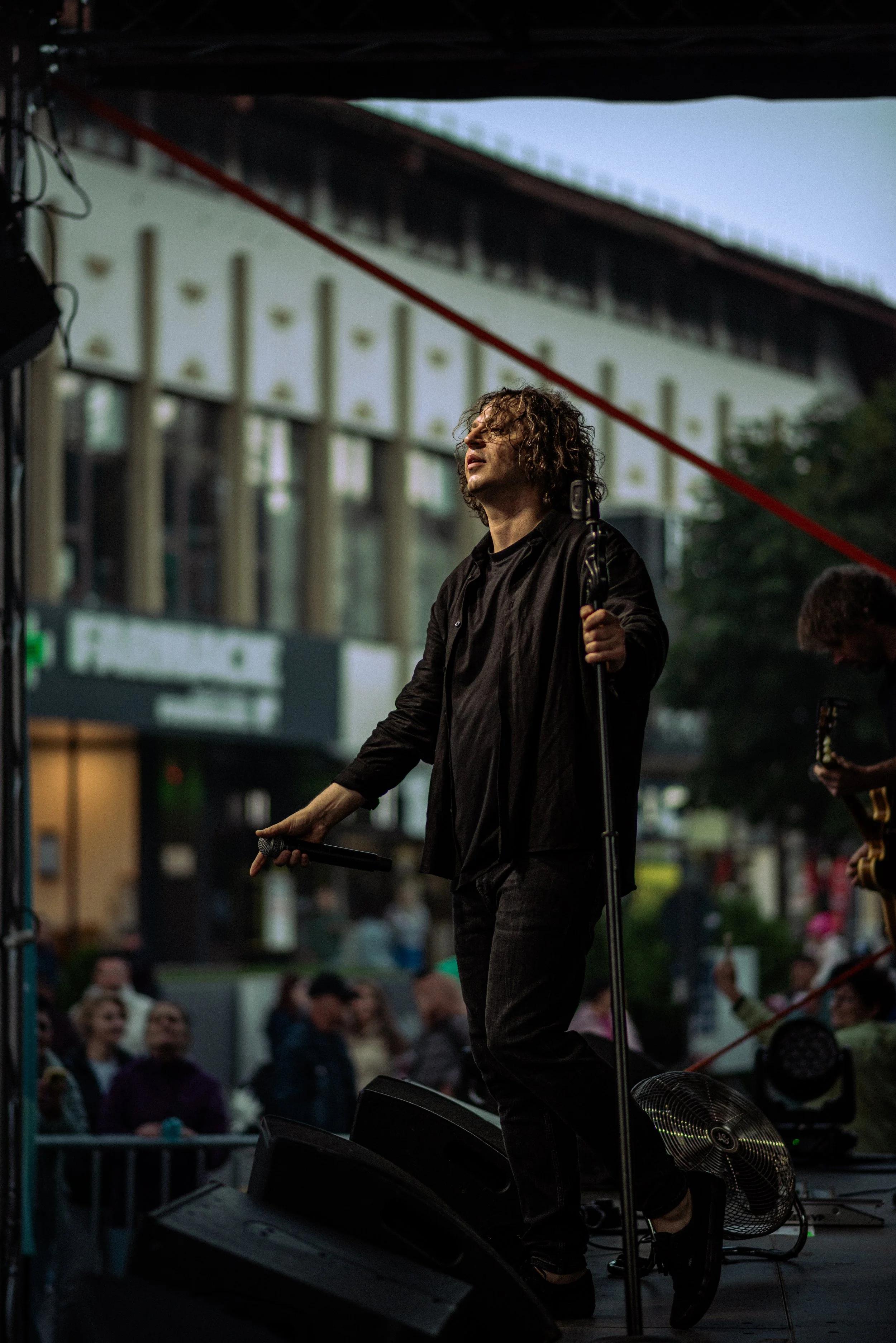 Musician performing on an outdoor stage with an audience watching.