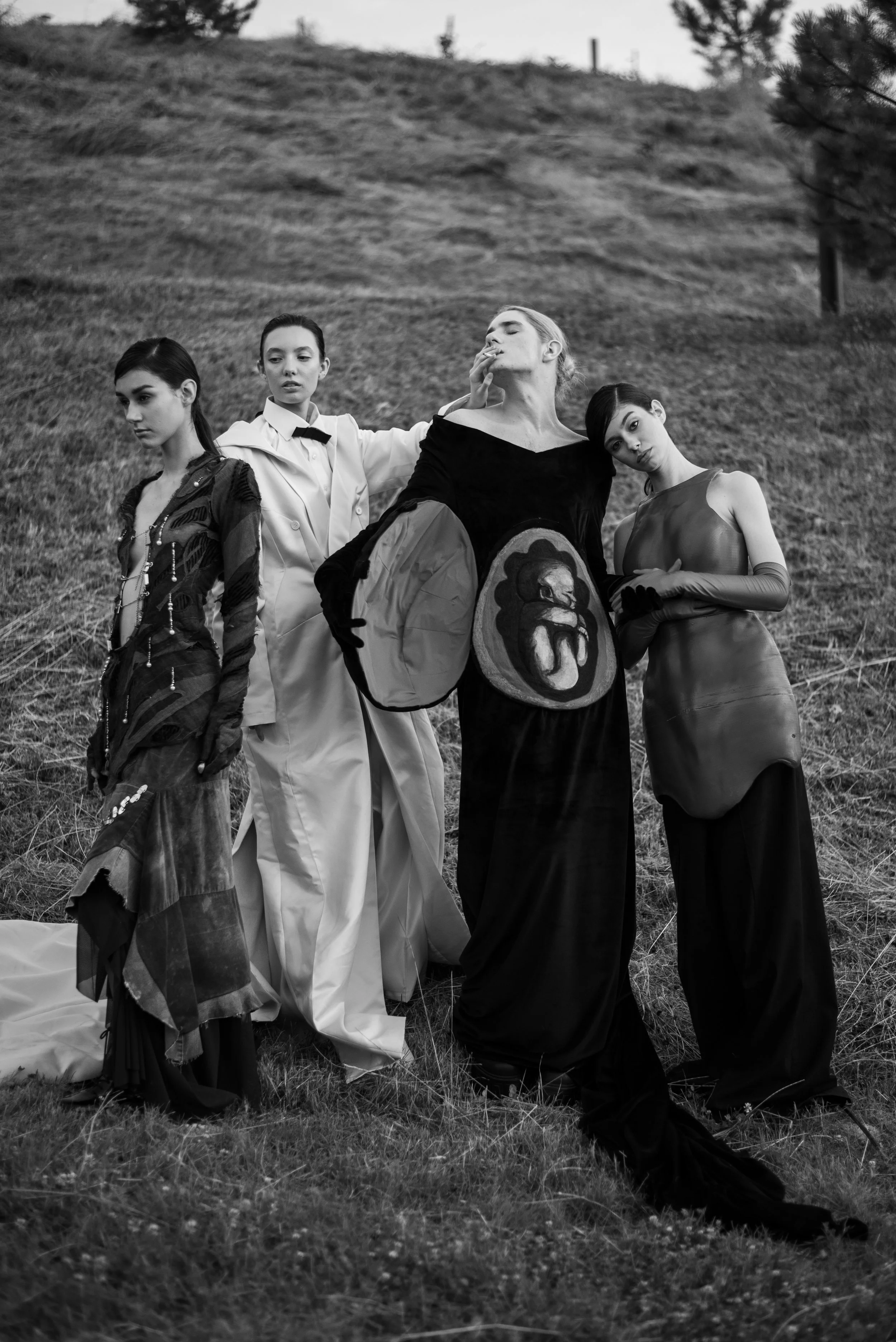 Four women standing outdoors on a grassy hillside, dressed in avant-garde fashion, with unique and artistic clothing and accessories.