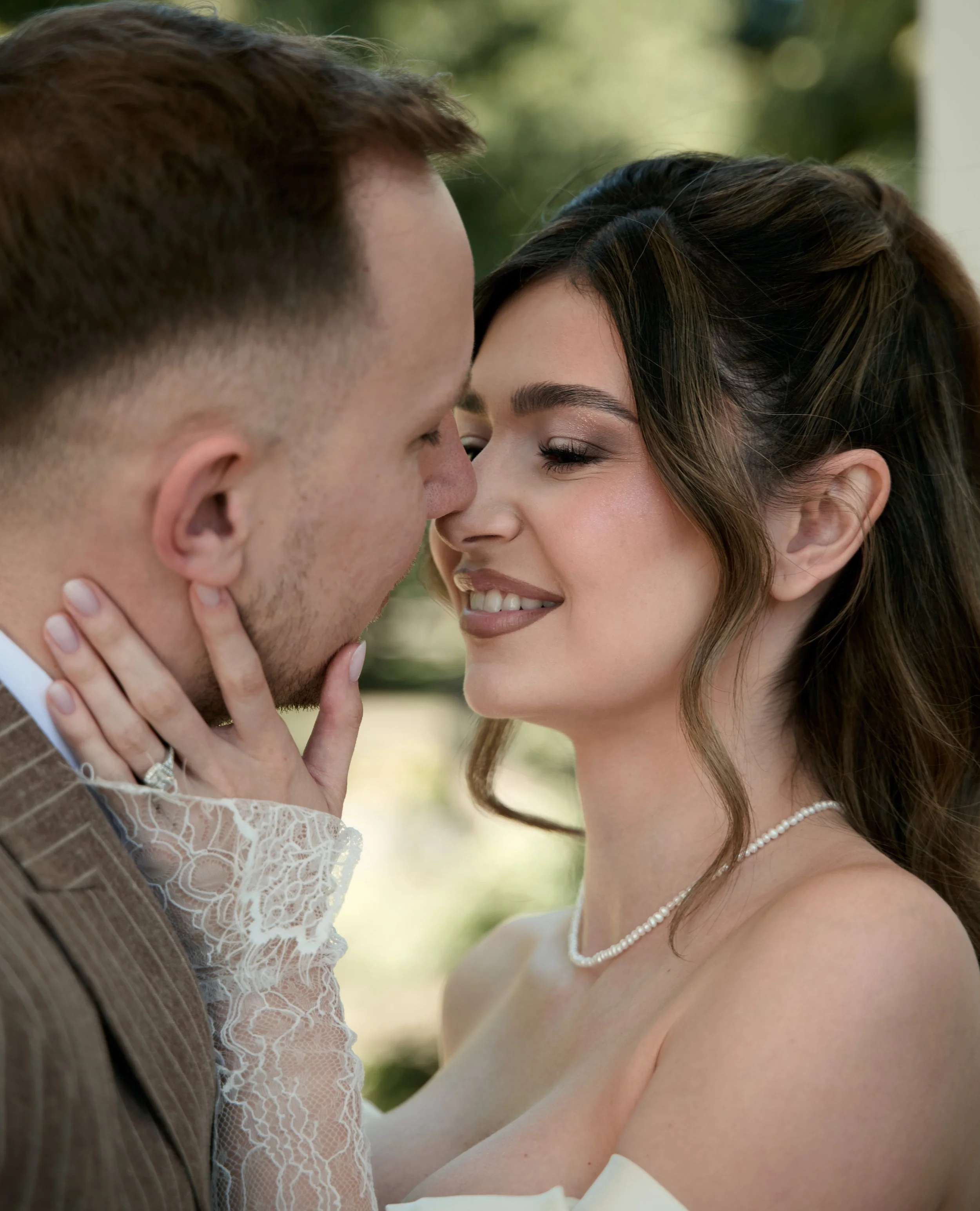 A close-up of a couple about to kiss, with the woman smiling with her eyes closed and the man holding her face gently.