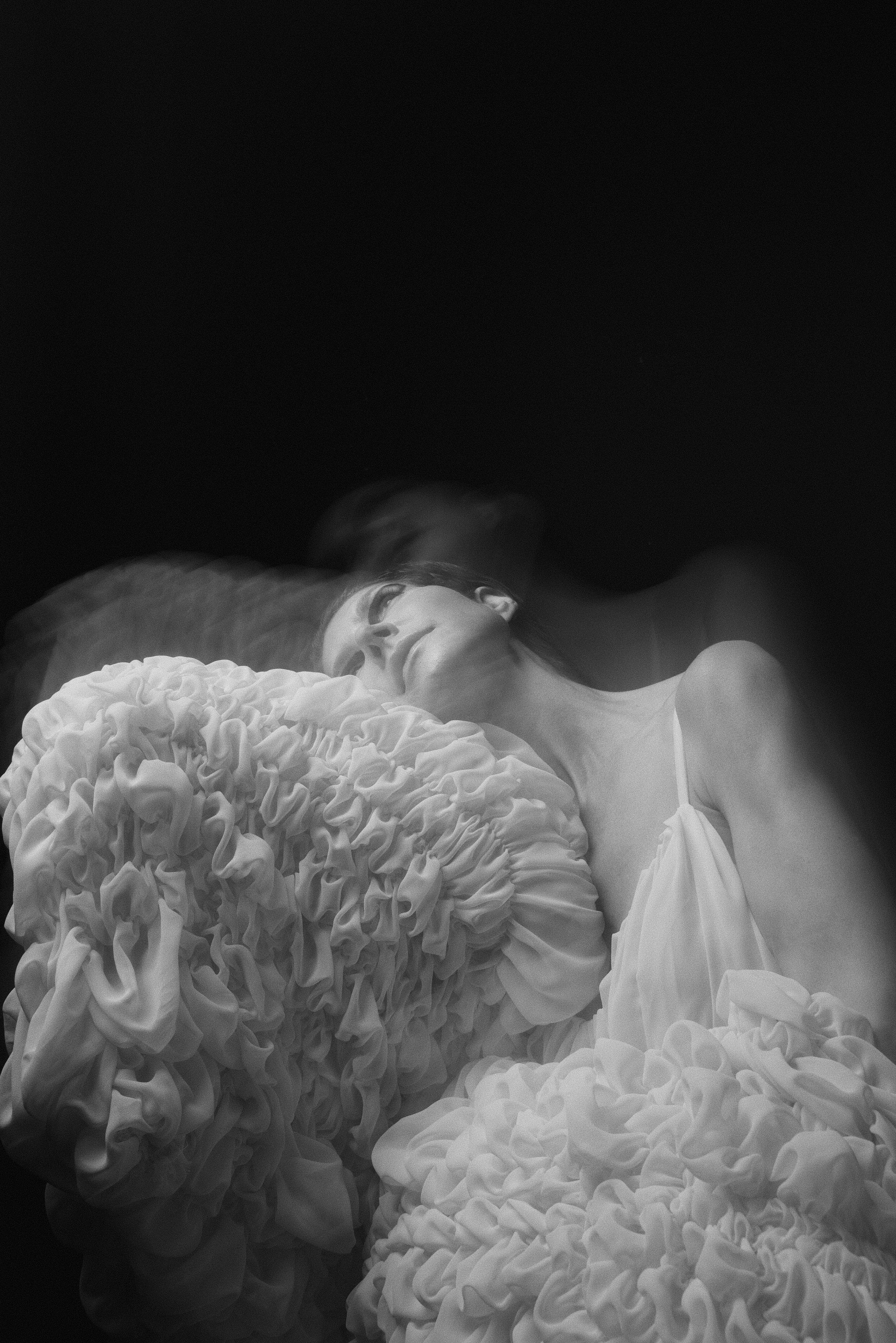 A woman sleeping on a pillow with ruffled fabric in black and white photograph.