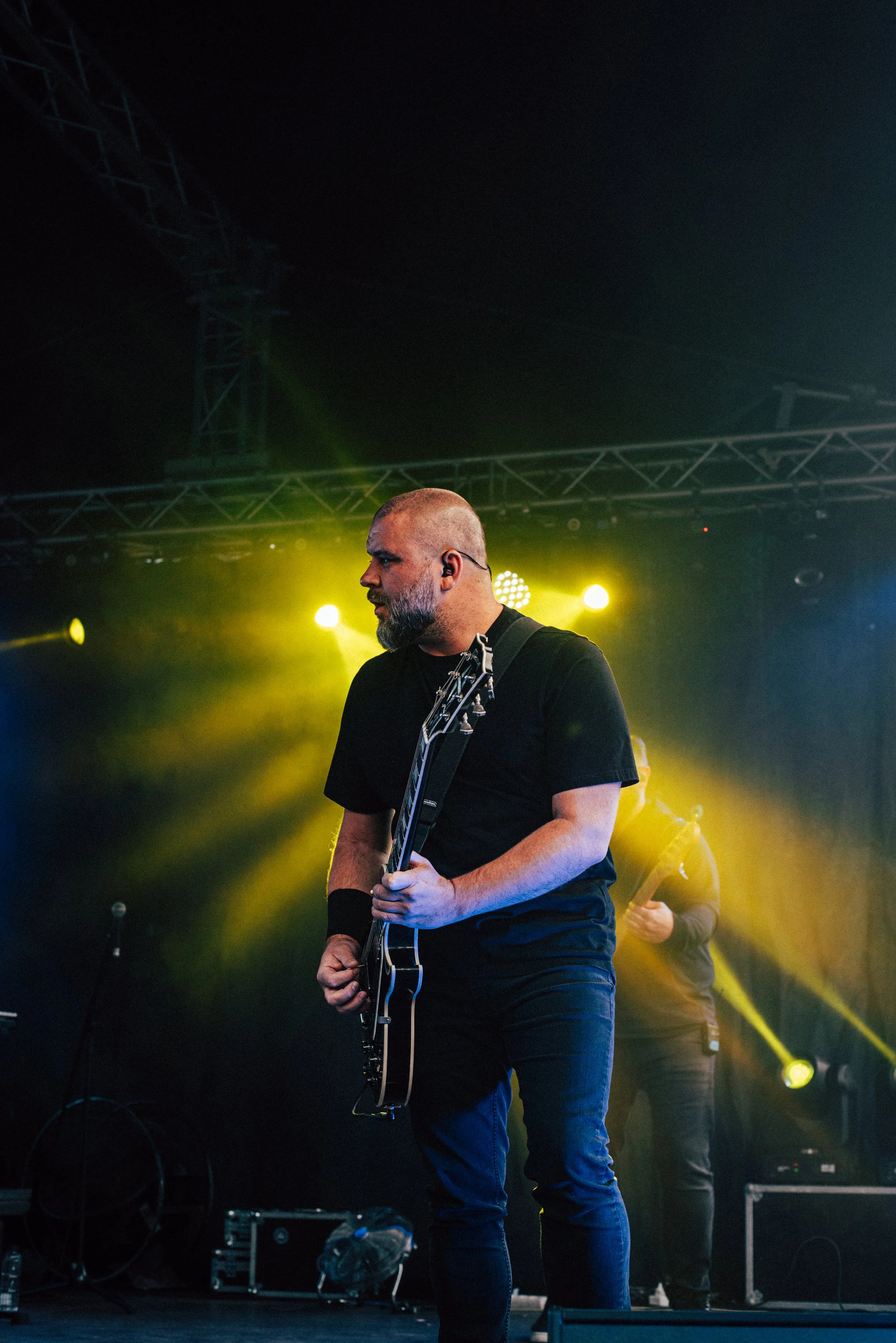 Guitarist performing on stage with yellow stage lighting and dark background.