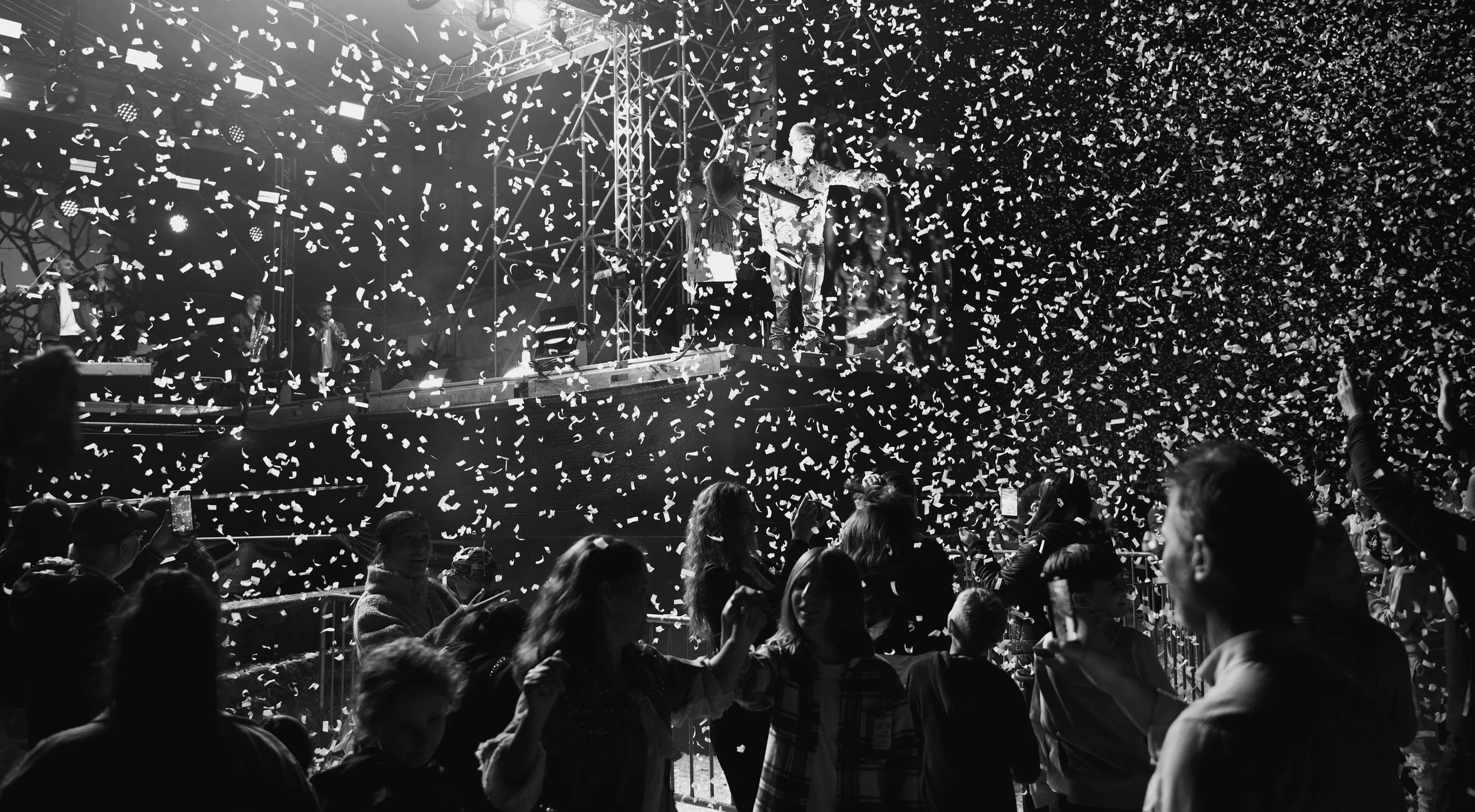 Crowd at concert celebrating with confetti, stage with performers in the background