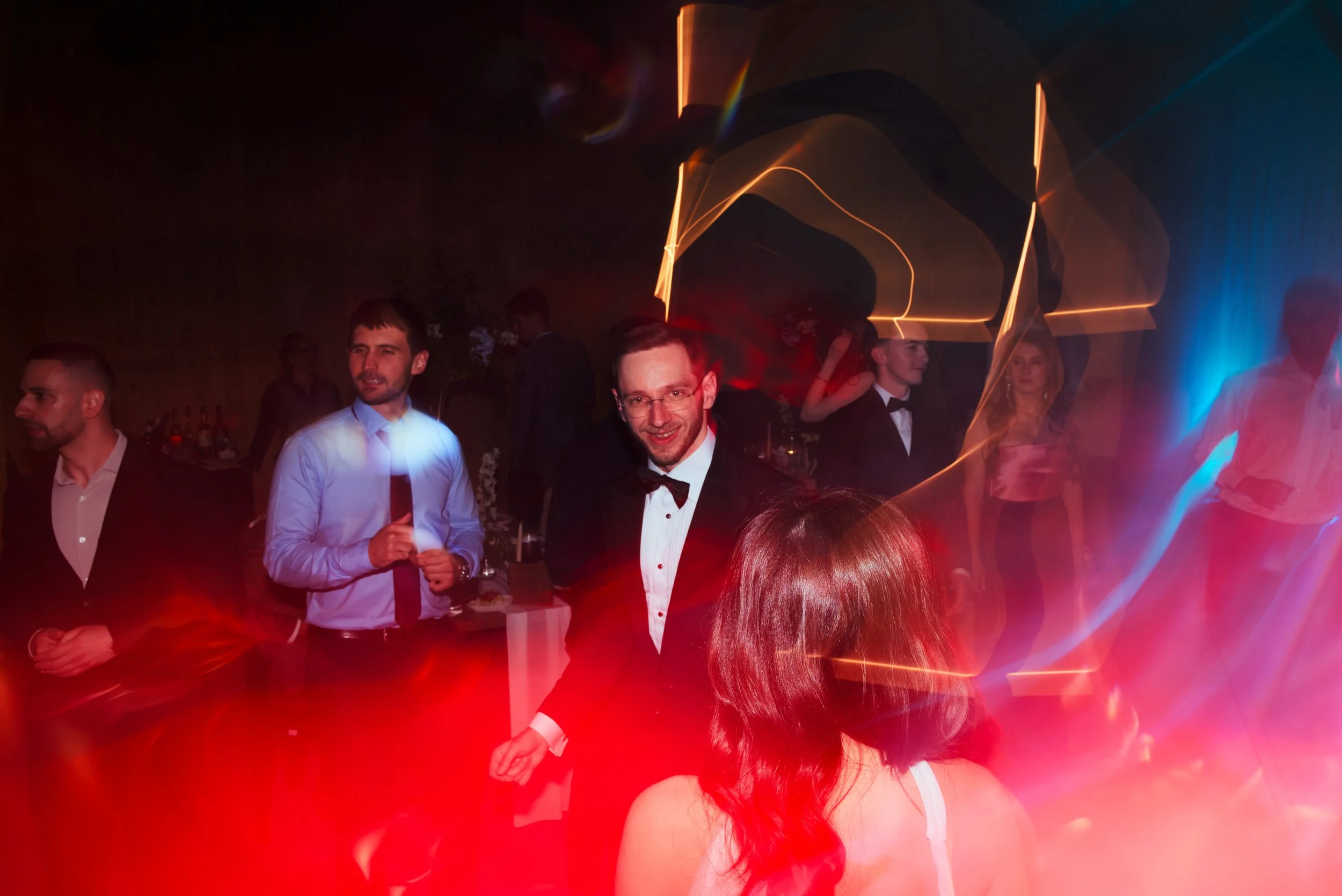 People dancing and socializing at a party with colorful lights and blurred motion effects.