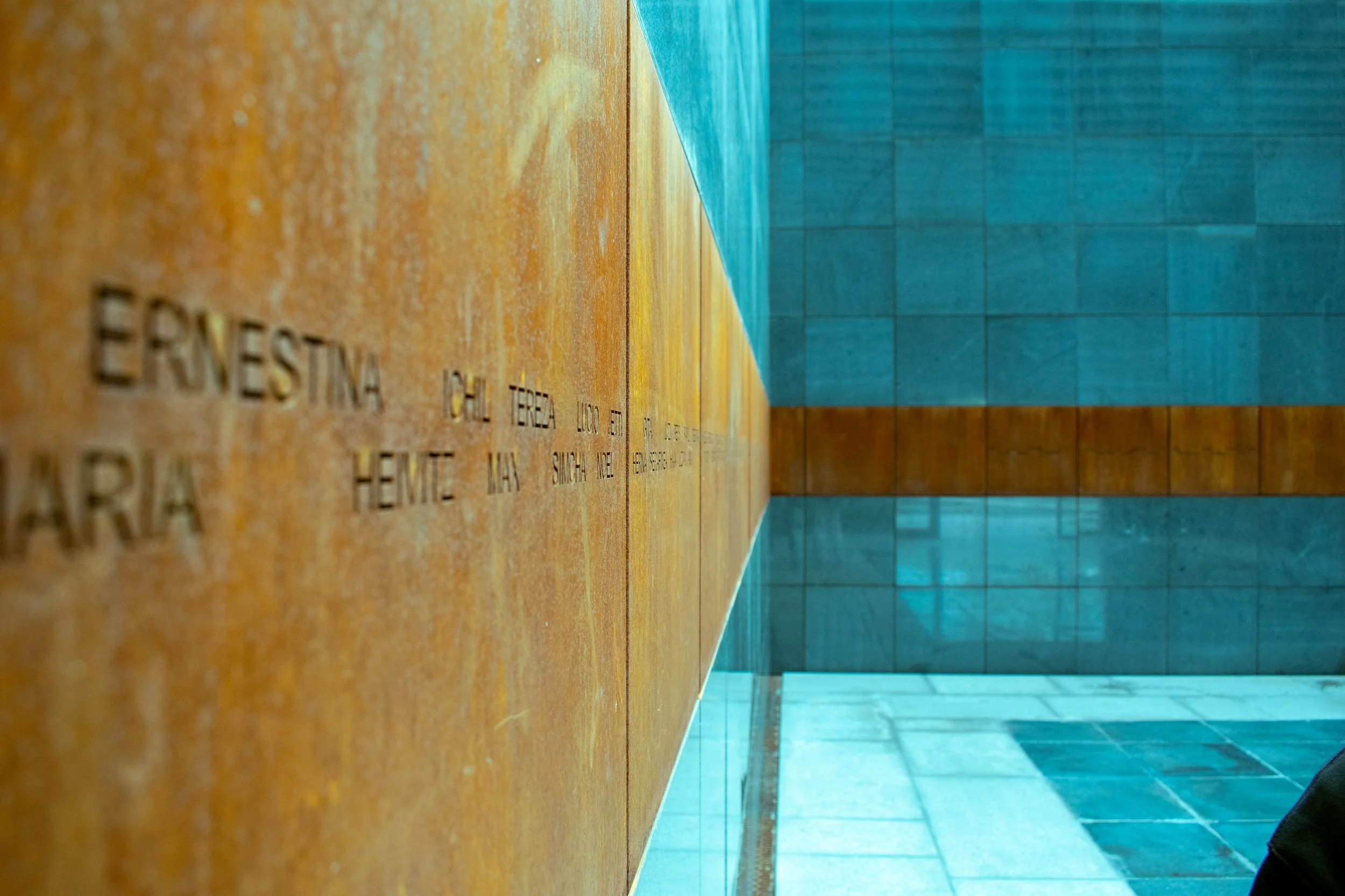 Close-up of a wall with engraved names, with a tiled wall and ceiling in the background.