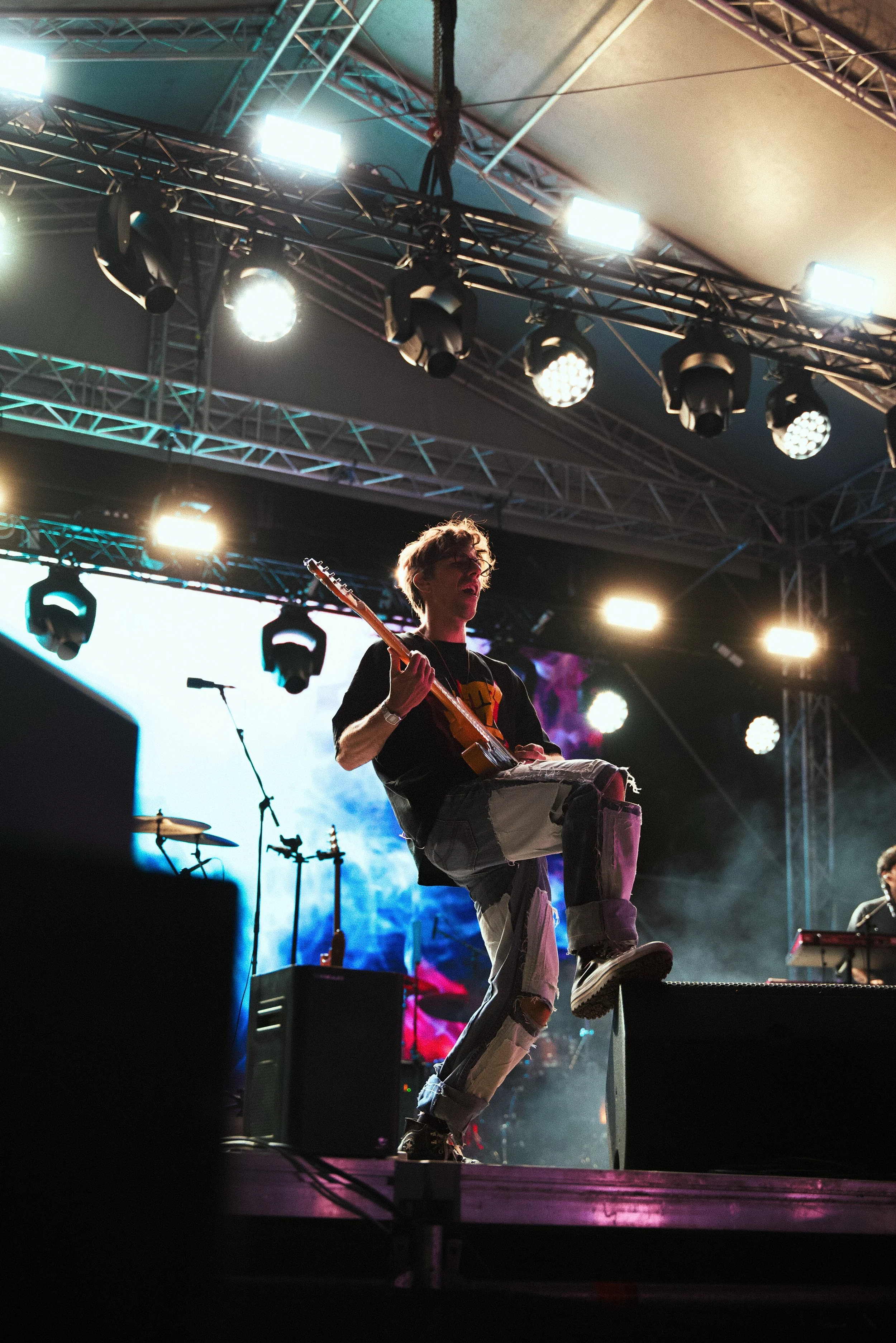 A musician playing an electric guitar on stage during a concert with bright stage lights and colorful background.