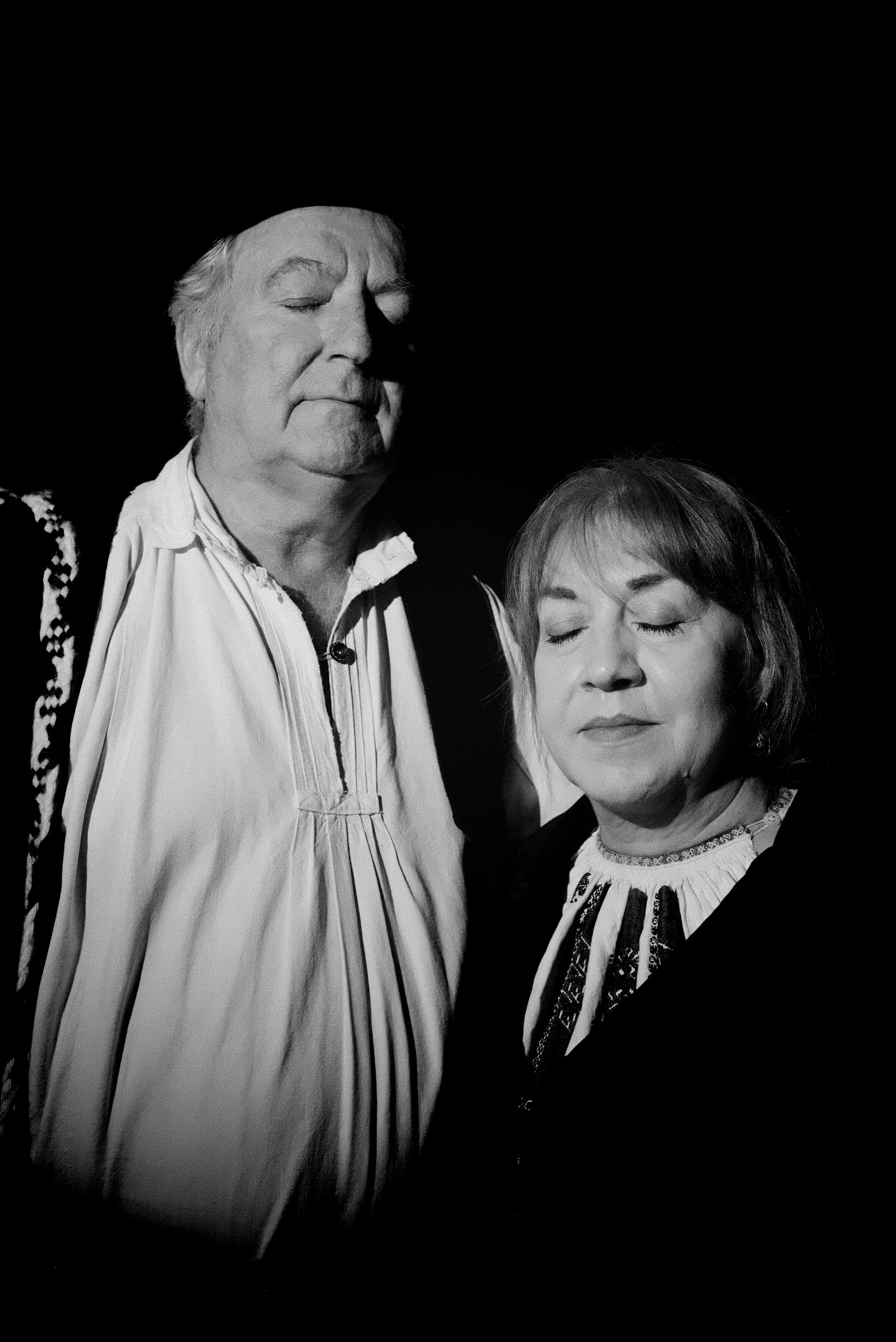 Black and white photo of an elderly man and woman with eyes closed, standing close together in a meditative or peaceful pose.