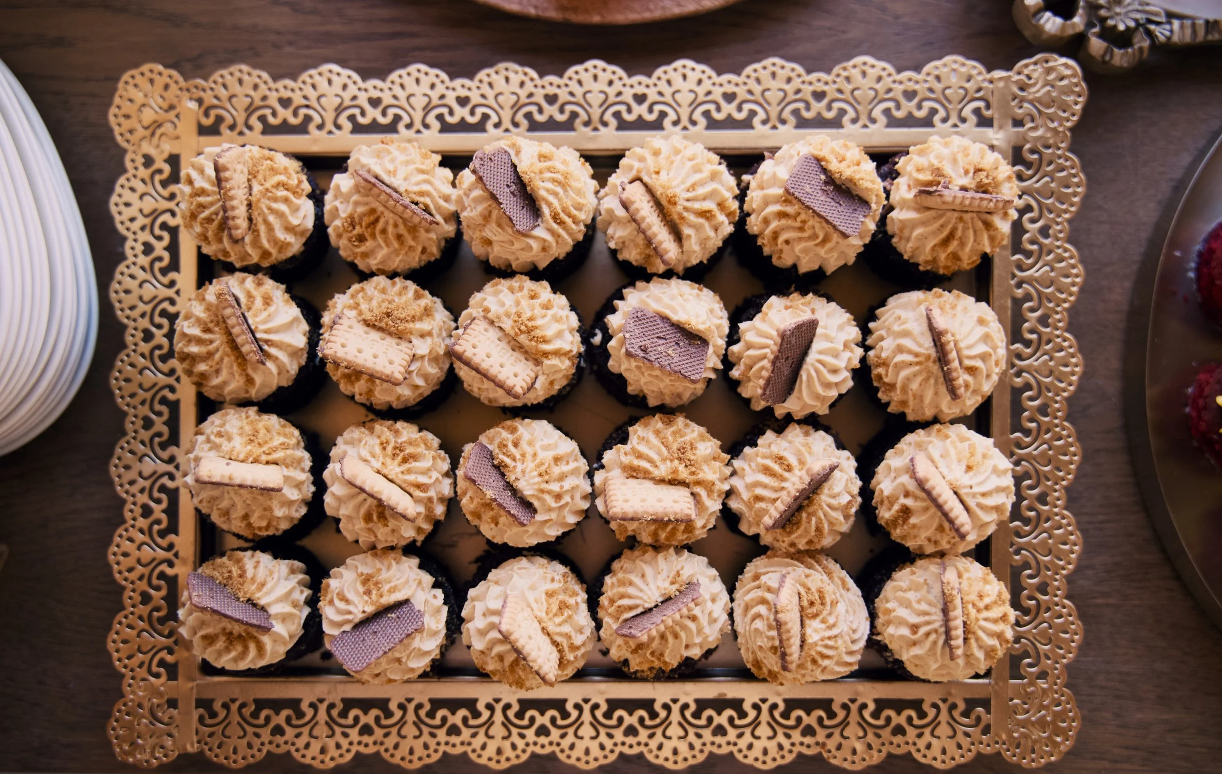 Tray of 20 cupcakes with beige frosting and cookie decorations.