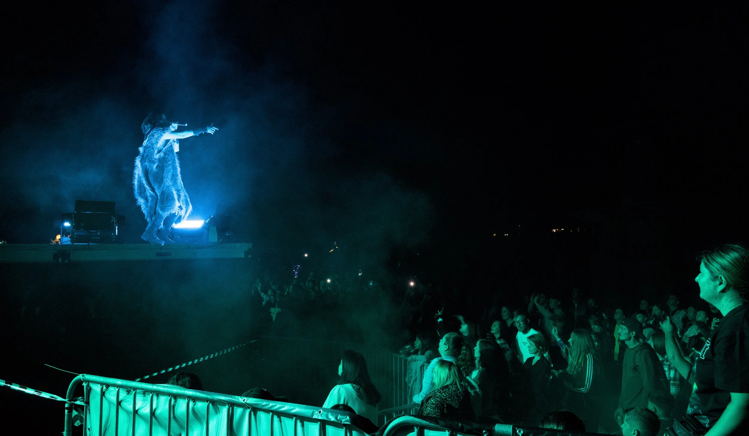 Performing artist on stage with a costume, illuminated by blue stage lighting, in front of a crowd at night.