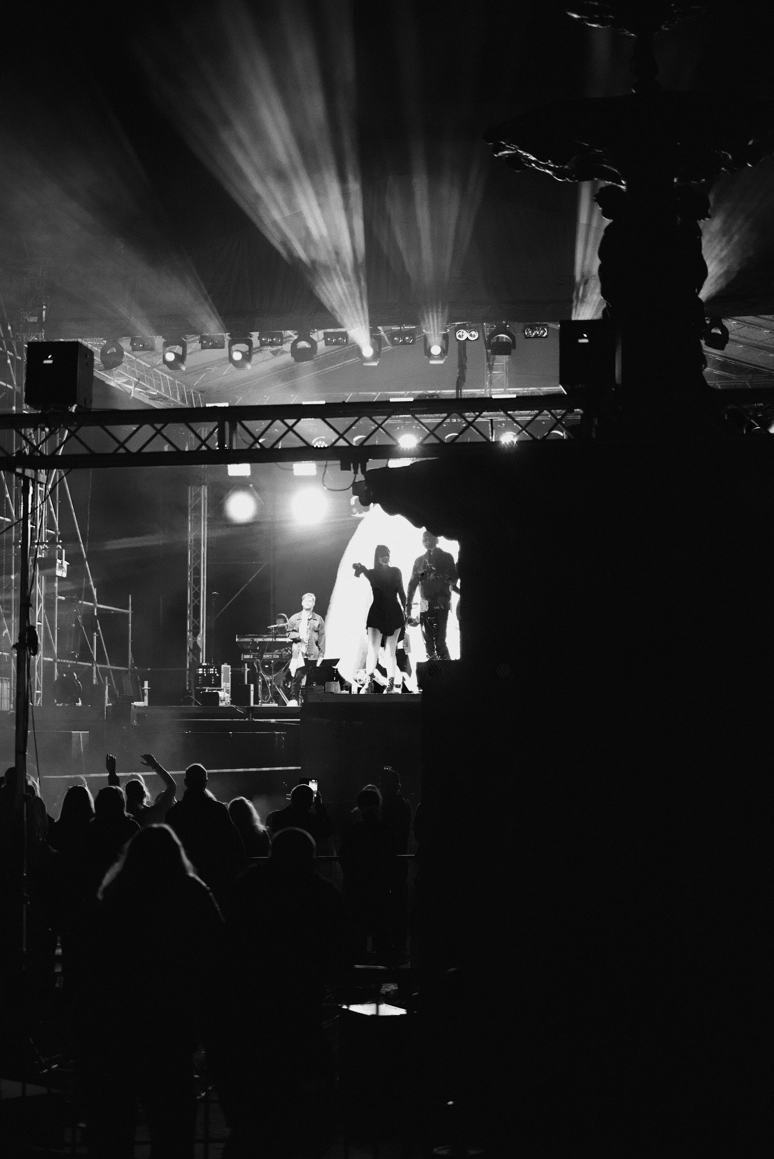 Black and white photo of a concert stage with performers and audience, stage lighting, and stage equipment.