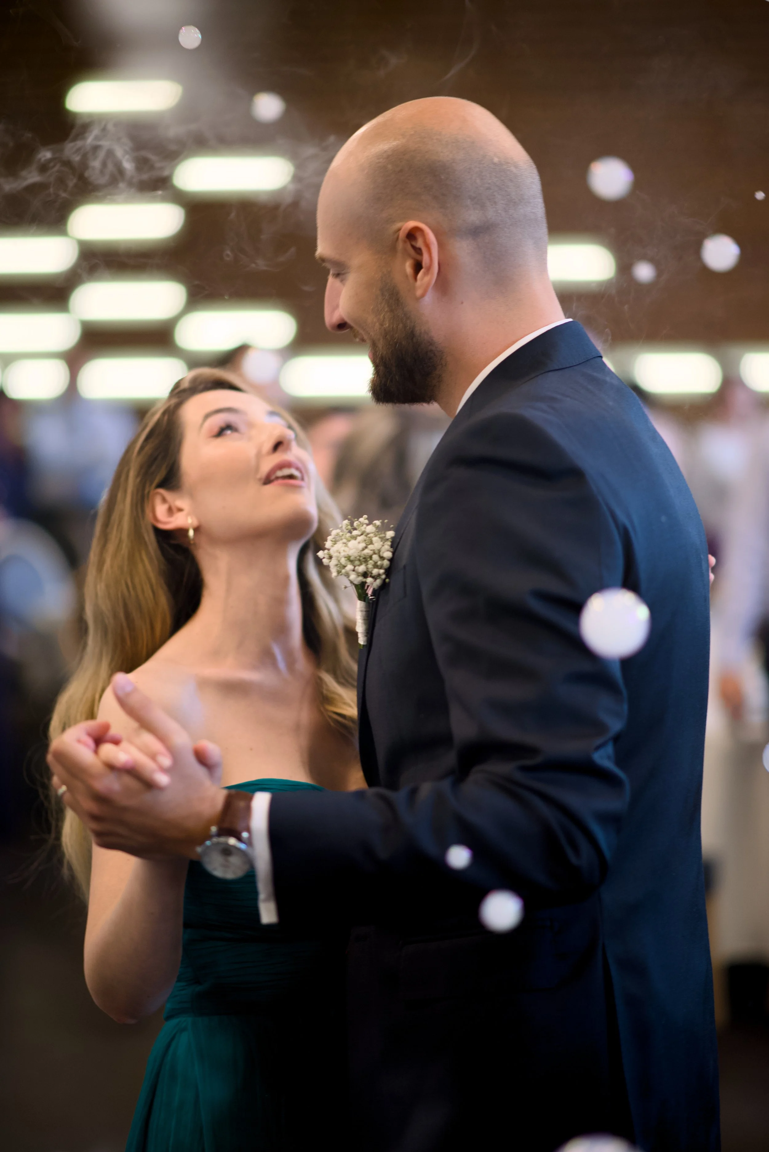 A couple dancing closely at a formal event, with the woman looking up at the man and the man smiling down at her.