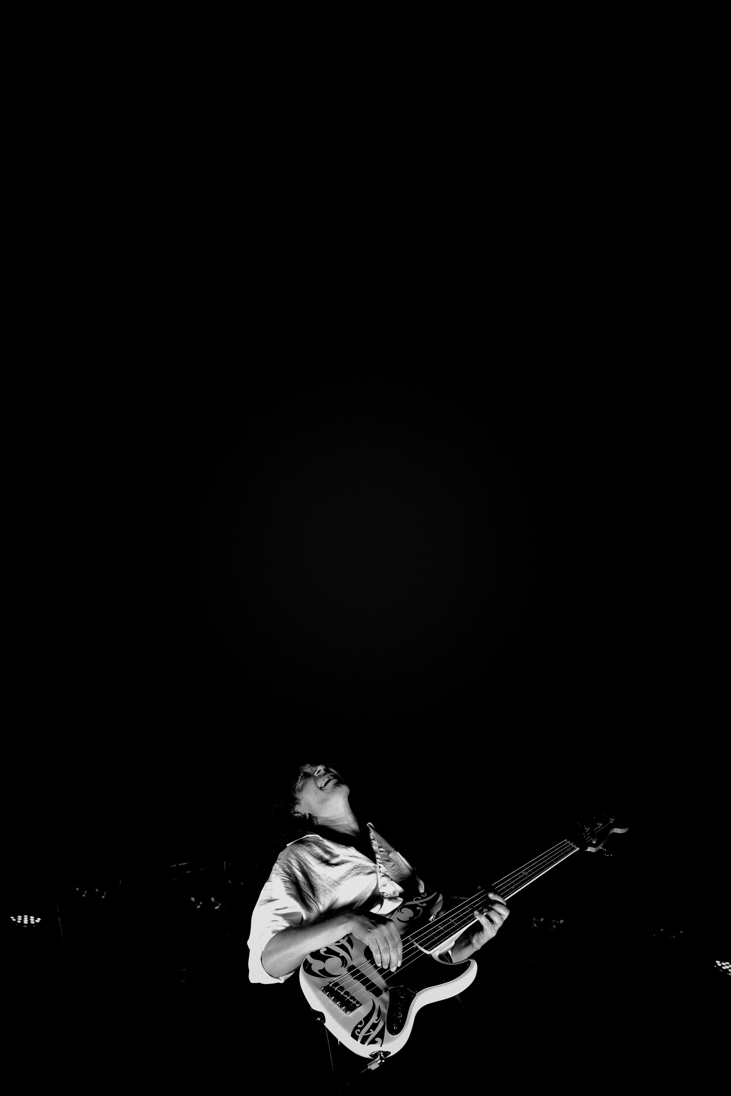 A female musician playing an electric guitar on stage, smiling and looking up, with a dark background.