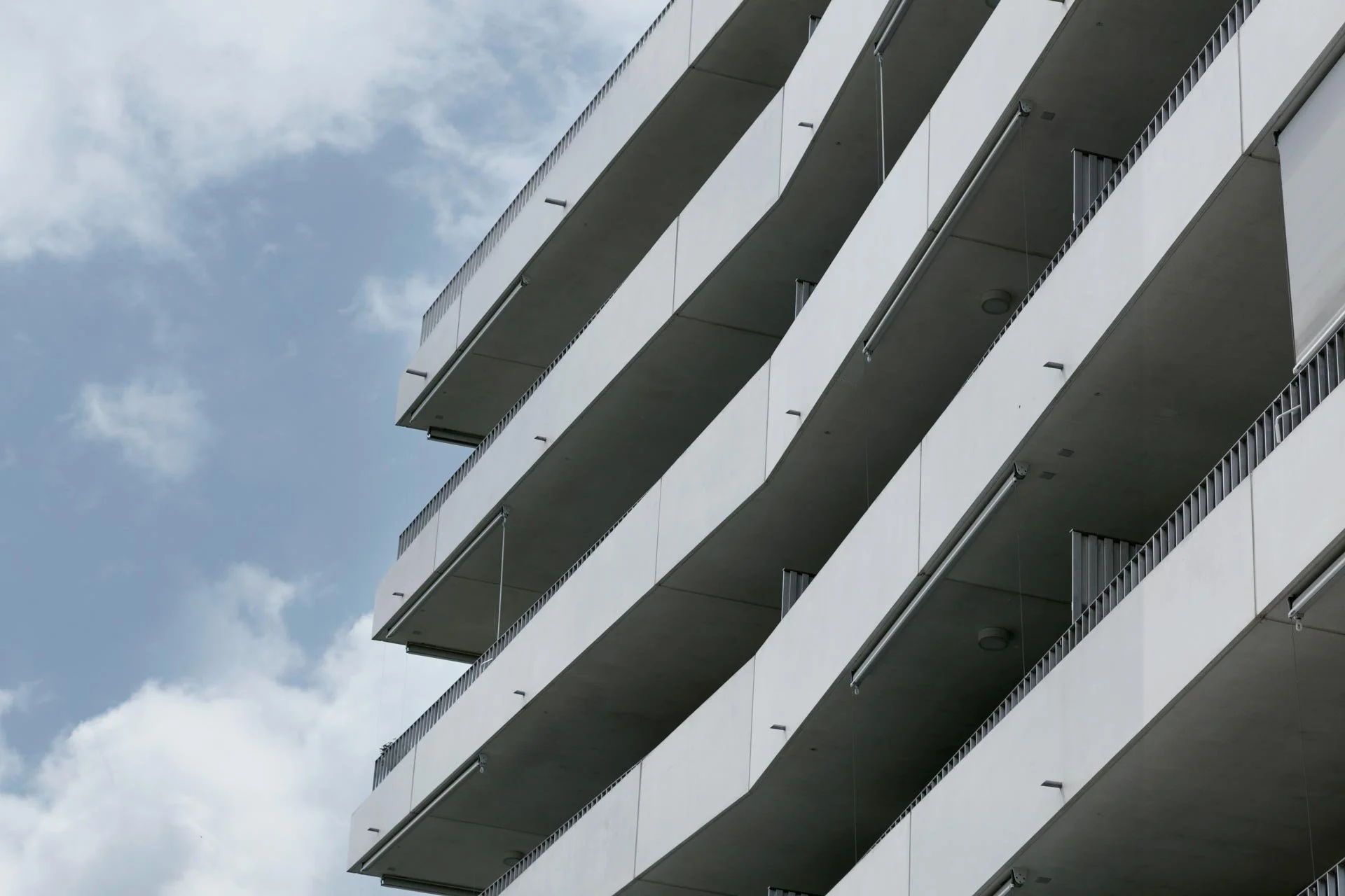 Façade d'un immeuble moderne avec plusieurs balcons en façade contre un ciel partiellement nuageux.