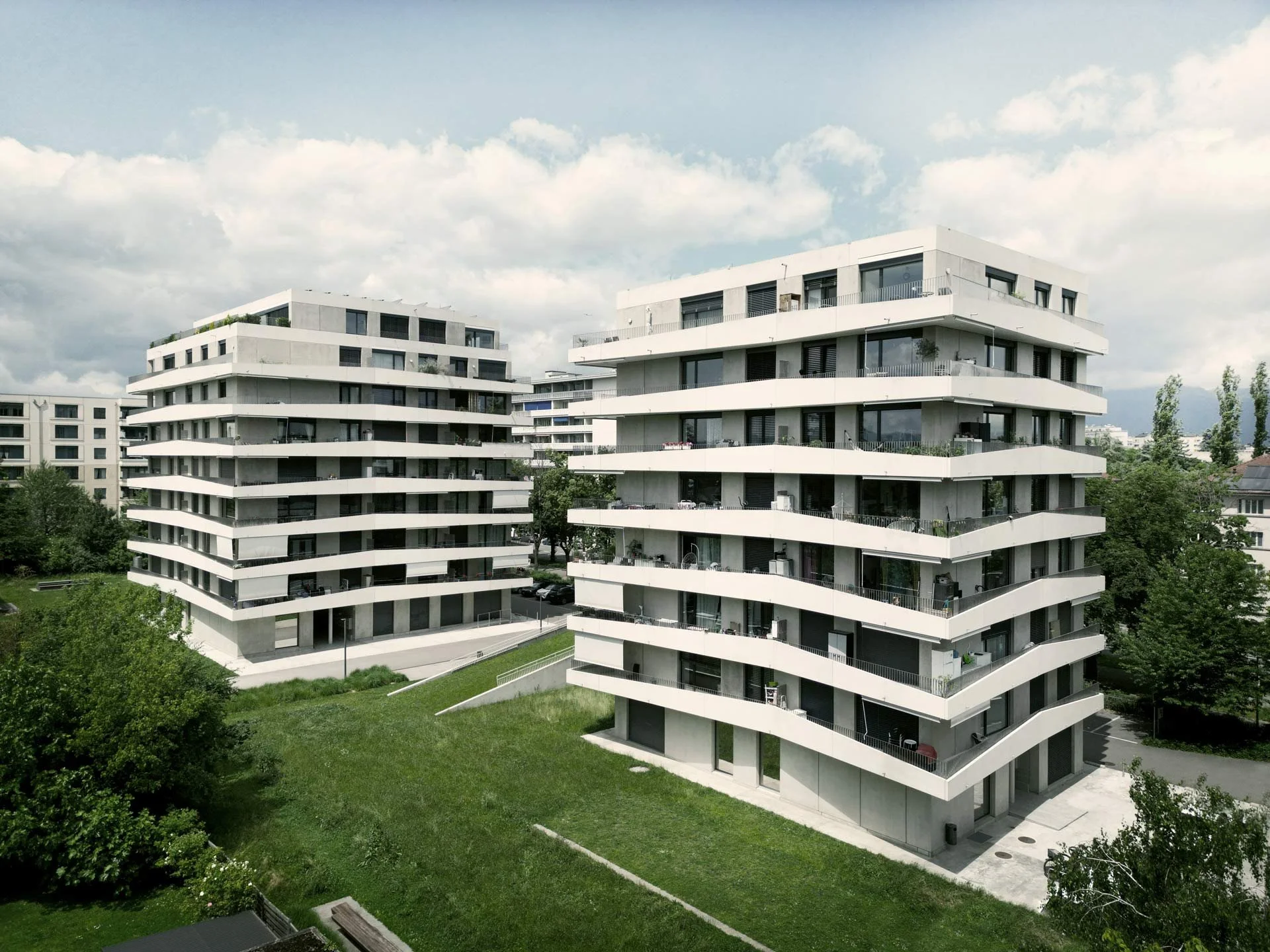 Deux immeubles résidentiels modernes avec balcons en courbe blanche, entourés d'espaces verts.