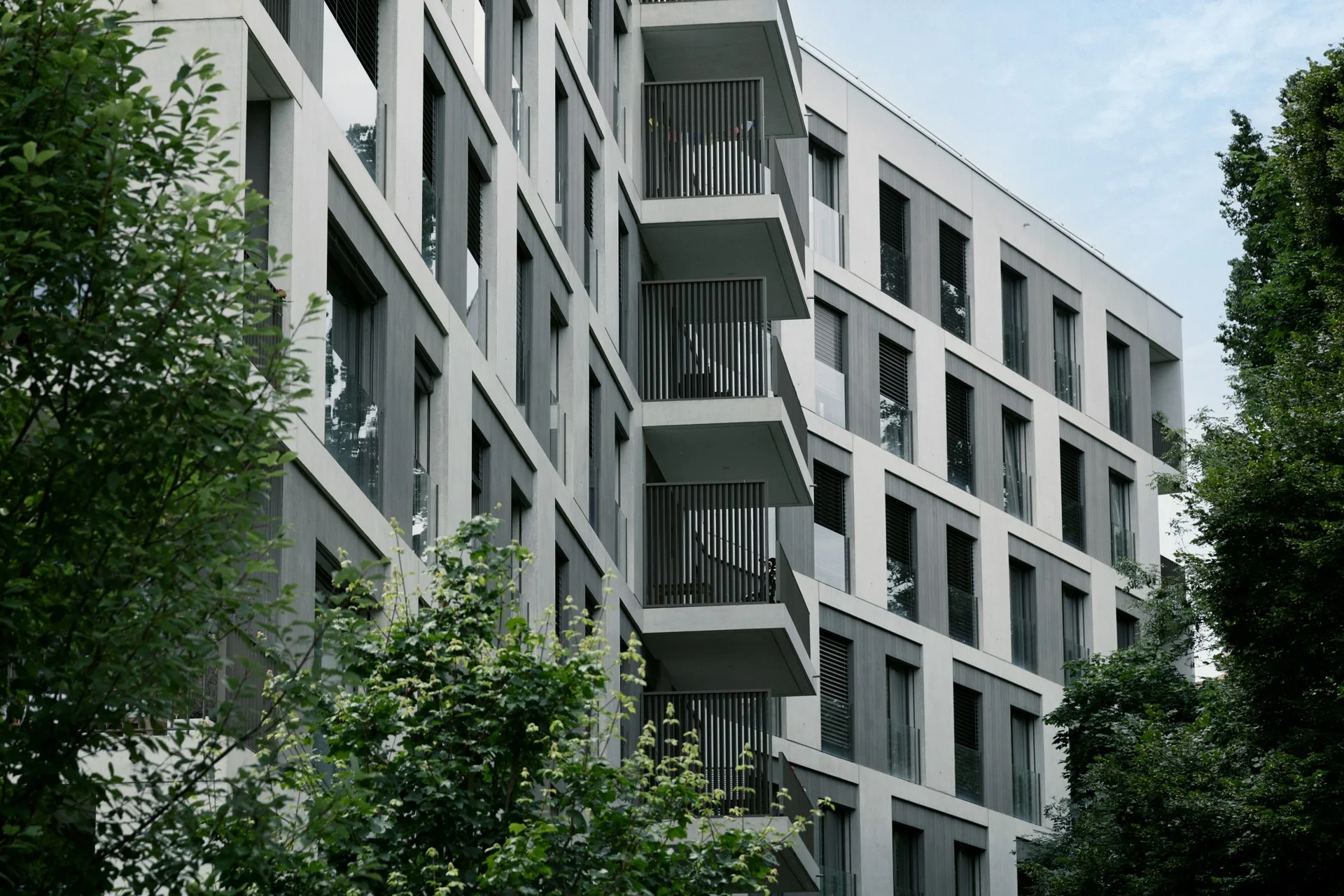 Façade d'un immeuble moderne avec plusieurs balcons et fenêtres, entourée d'arbres.
