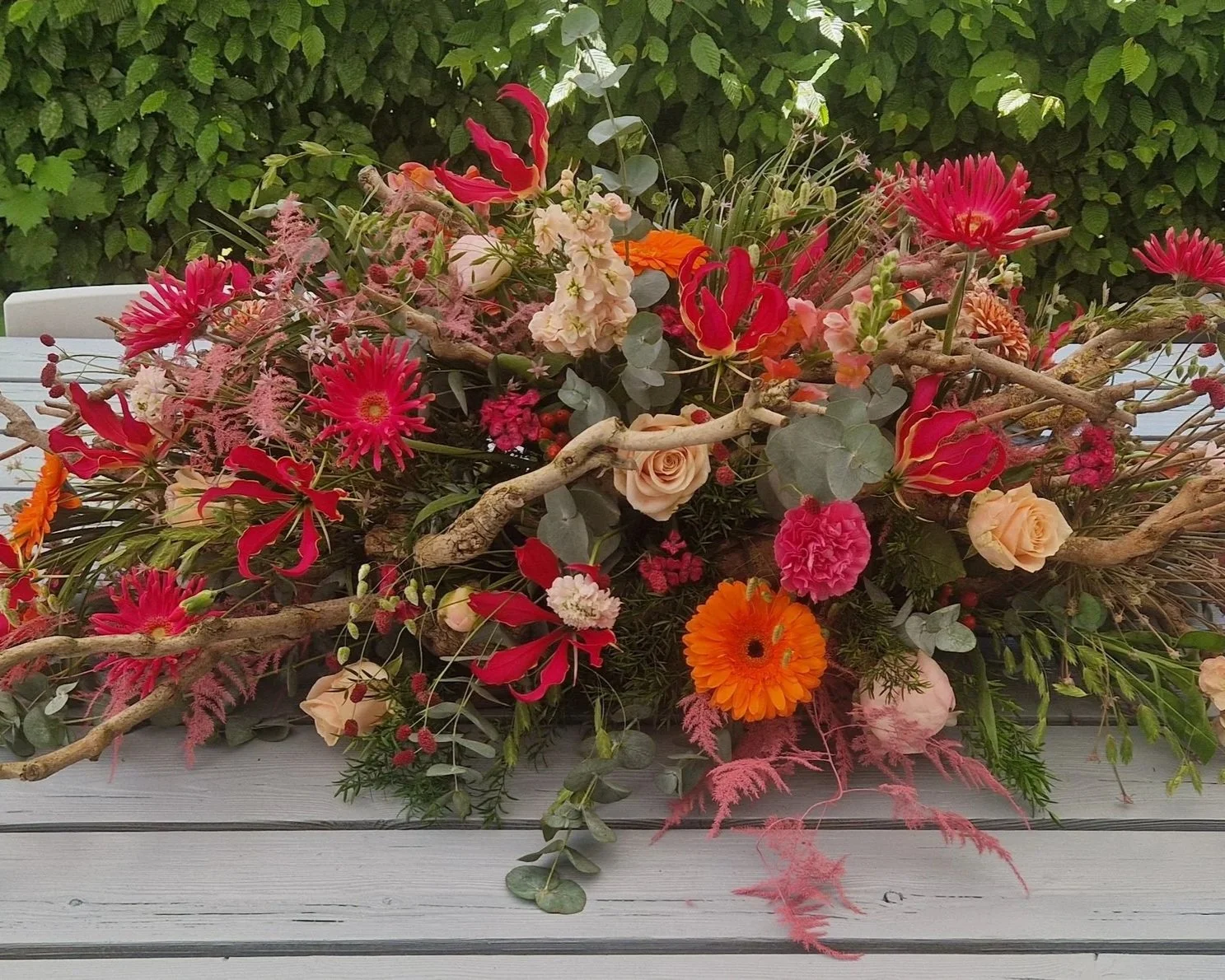 Langwerpig rouwbloemstuk met rode, oranje en roze bloemen.jpg