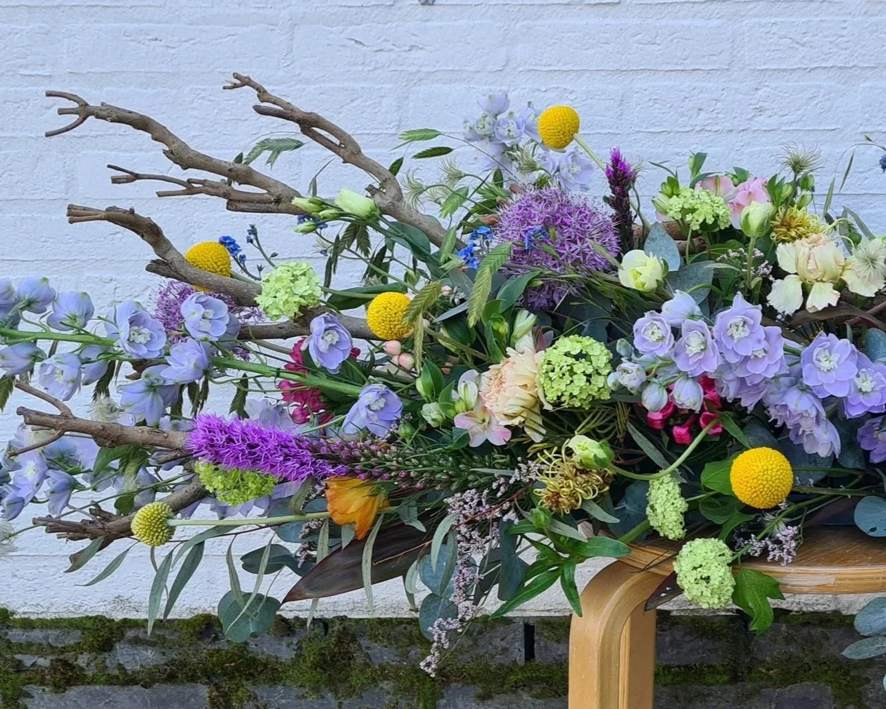 Natuurlijk rouwbloemstuk met lila bloemen, takken en gele accenten.jpg