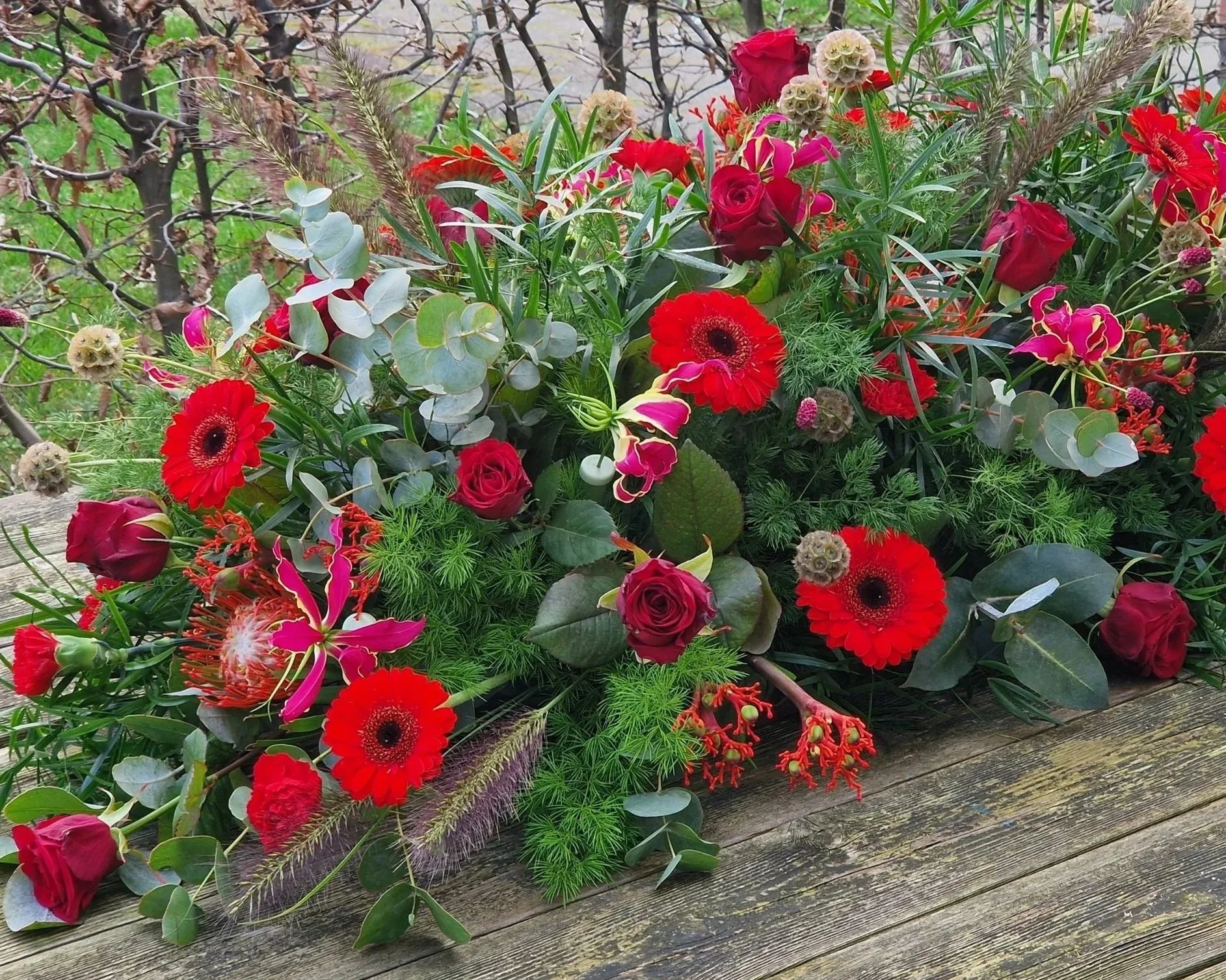Langwerpig rouwbloemstuk met rode bloemen en veel groen.jpg